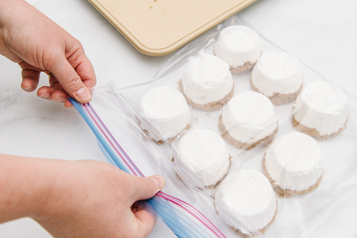 Two hands zipping up a resealable bag of 9 plain mini cheesecakes.