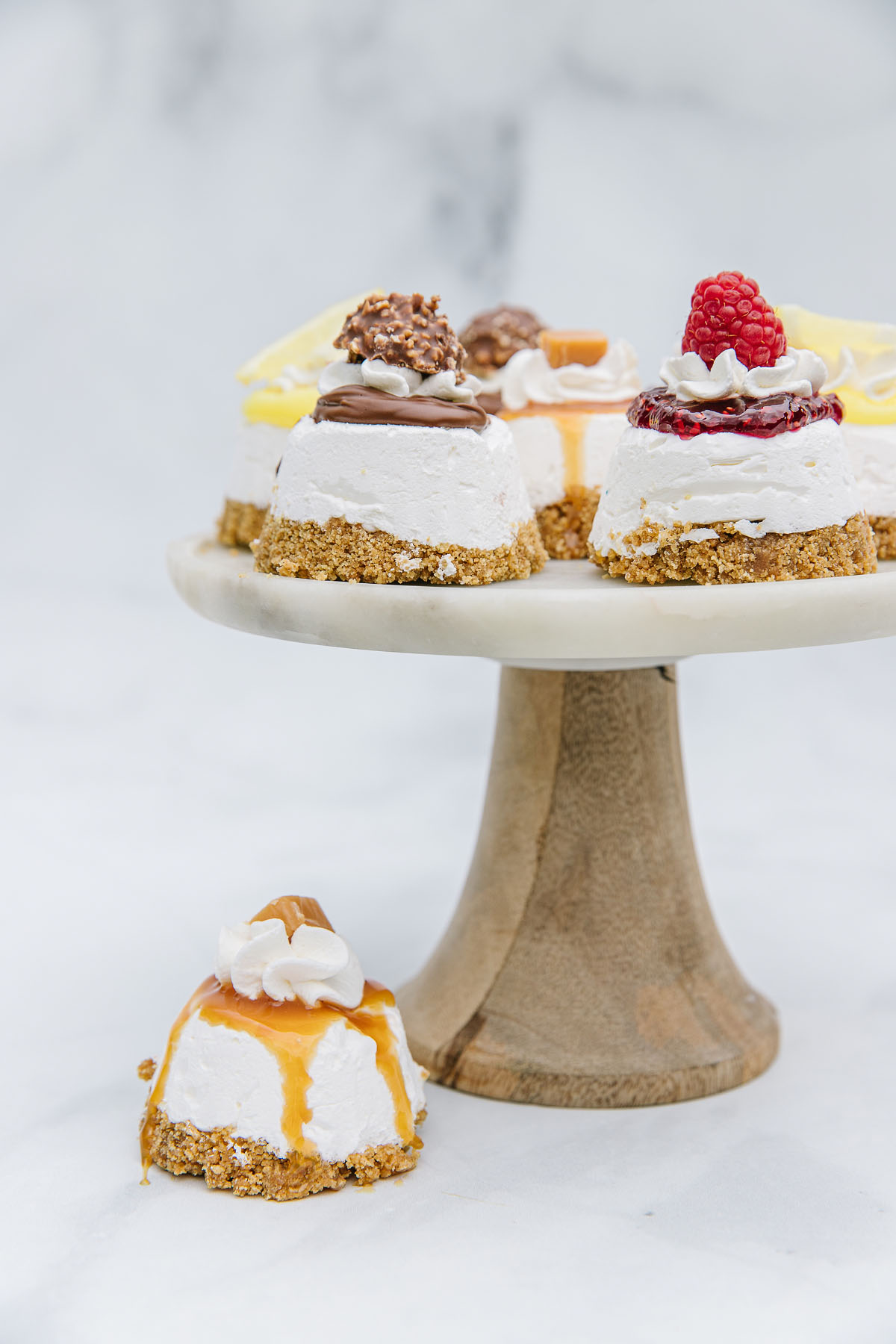 A wooden pedestal with various mini cheesecakes and one cheesecake underneath it.