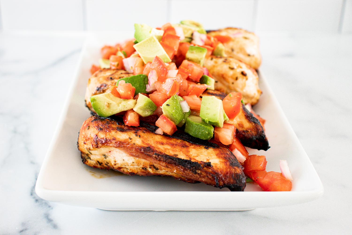 White dishes of cilantro lime grilled chicken with avocado salsa