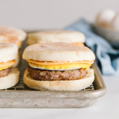 sausage mcmuffin copycat recipe - 4 sandwiches on a baking pan with eggs in background