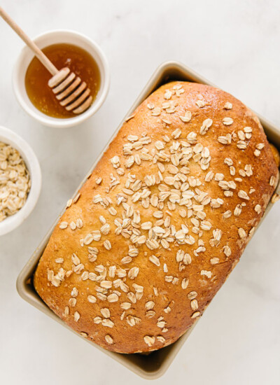 Loaf of honey oat bread in a bread pan with honey and oats.