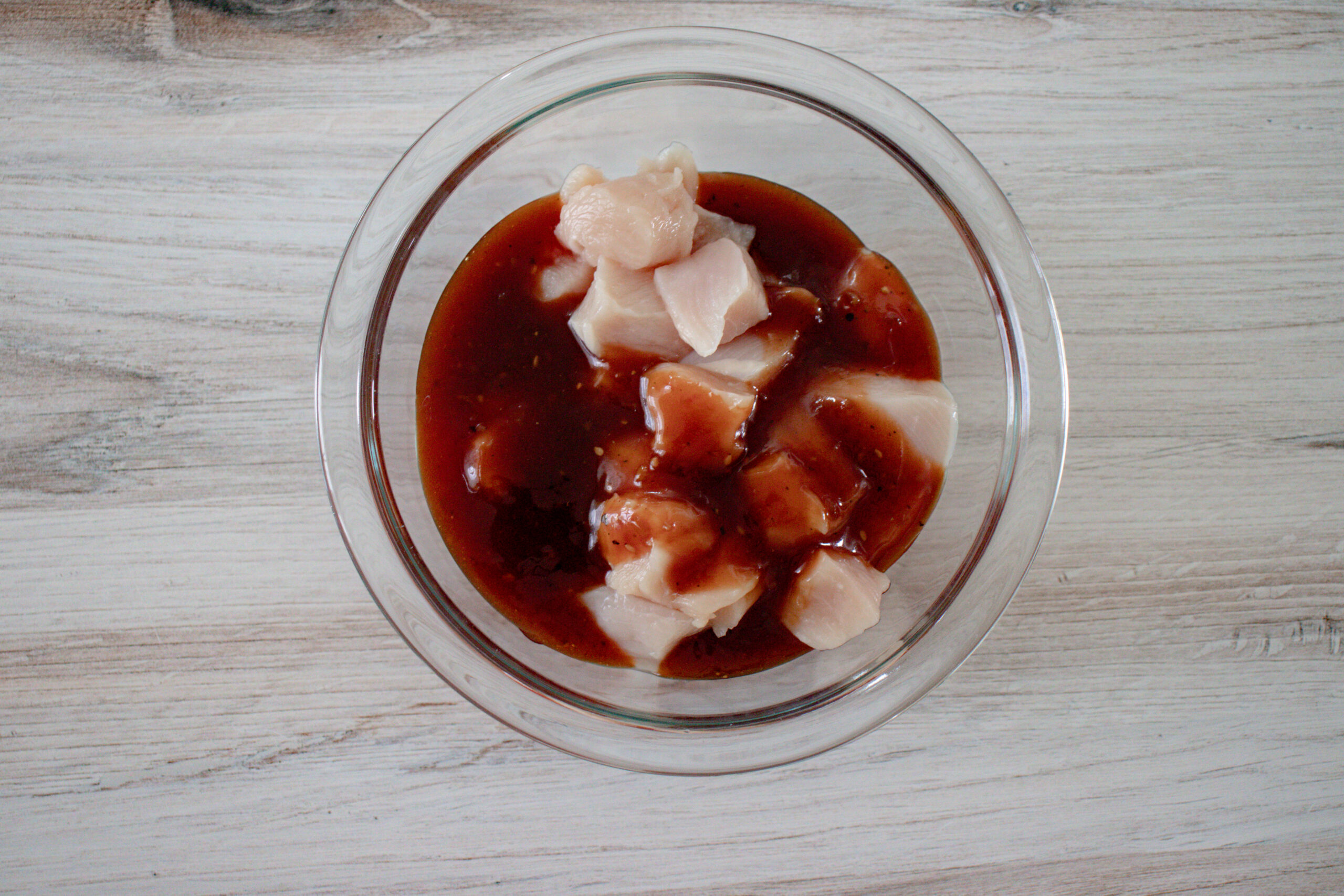 A glass bowl of chicken marinating in sauce.