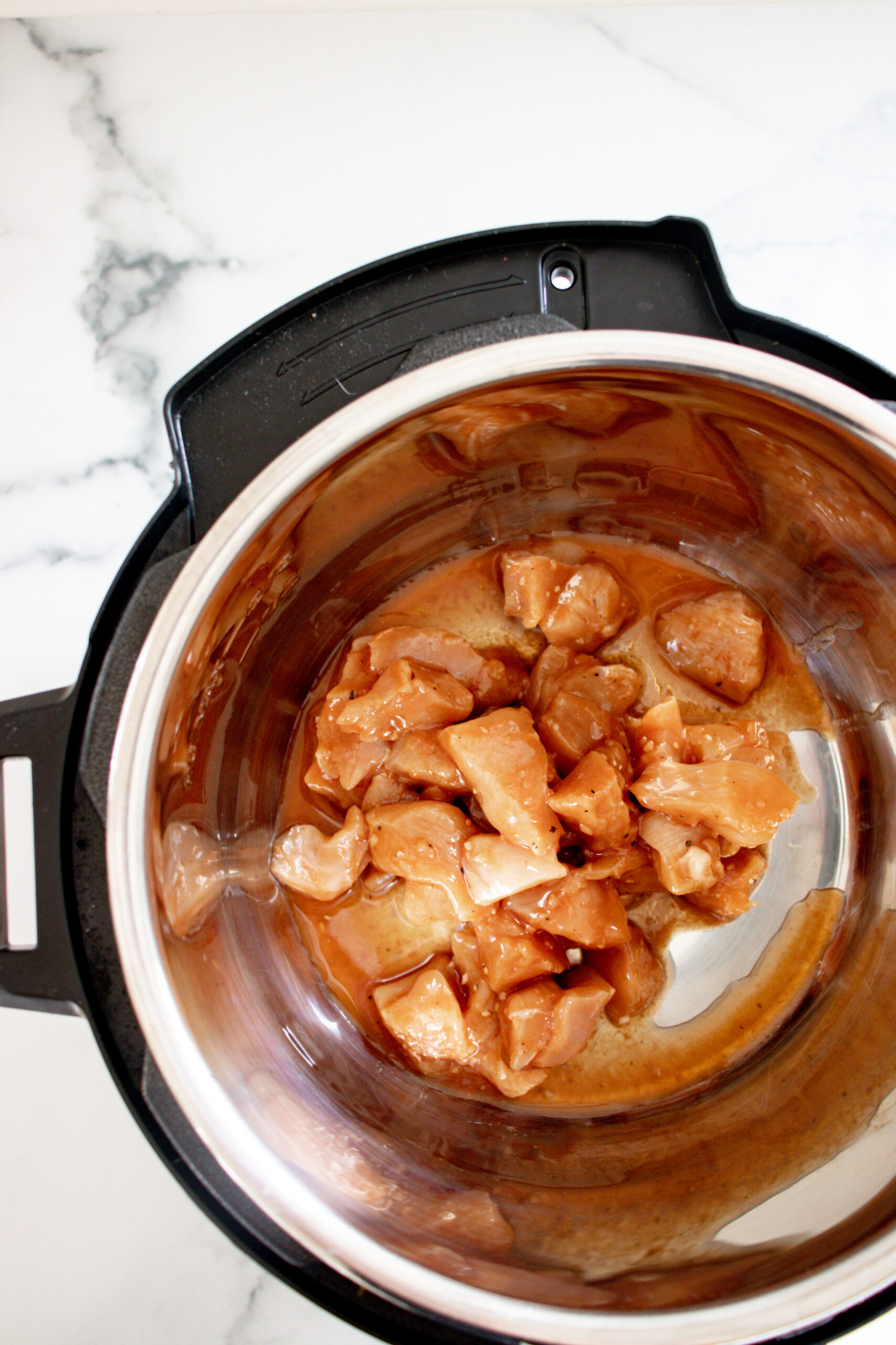 An Instant Pot with raw chicken and sauce in it.