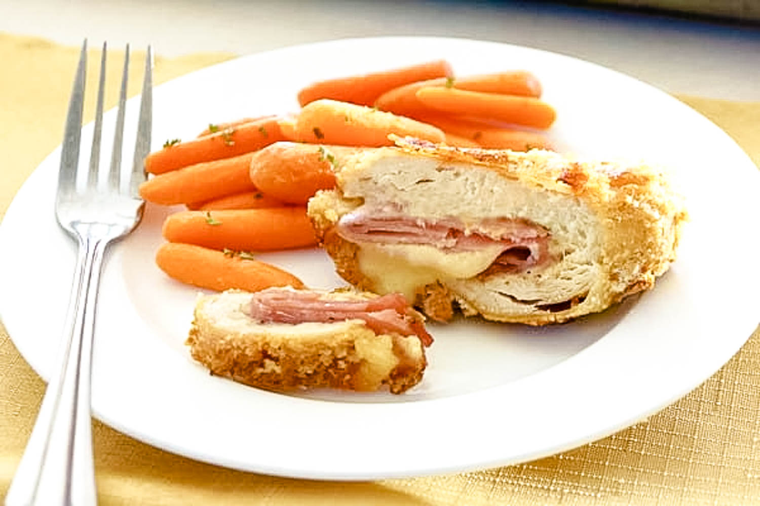 A white plate with chicken cordon bleu with carrots on the plate and a metal plate.