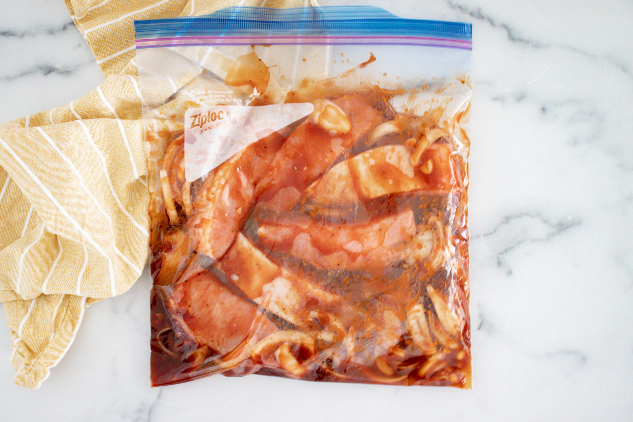 A gallon size resealable bag with uncooked ribs and sauce in it.