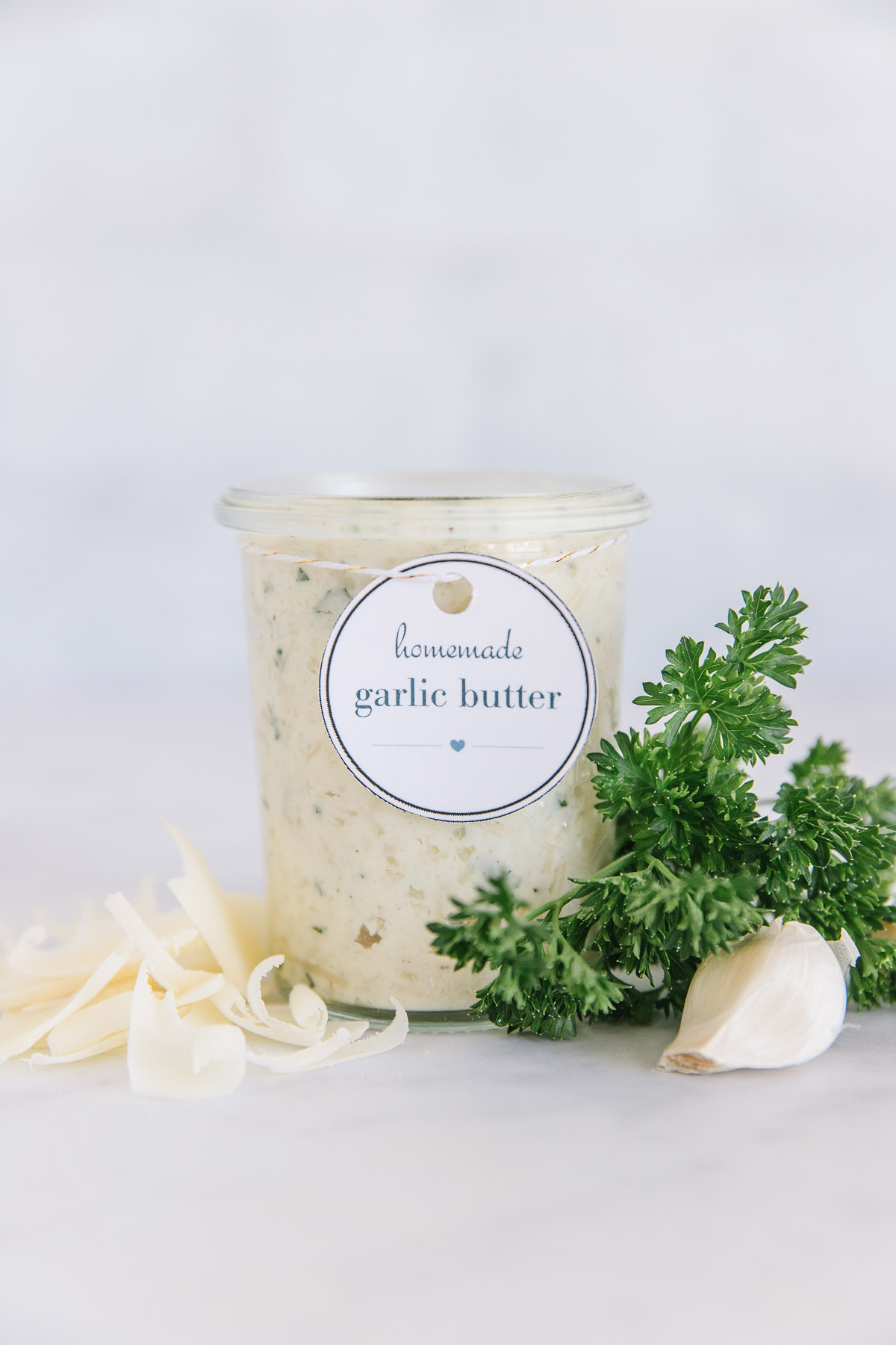 A container of homemade garlic butter with label with garlic and cheese and herbs on the side.
