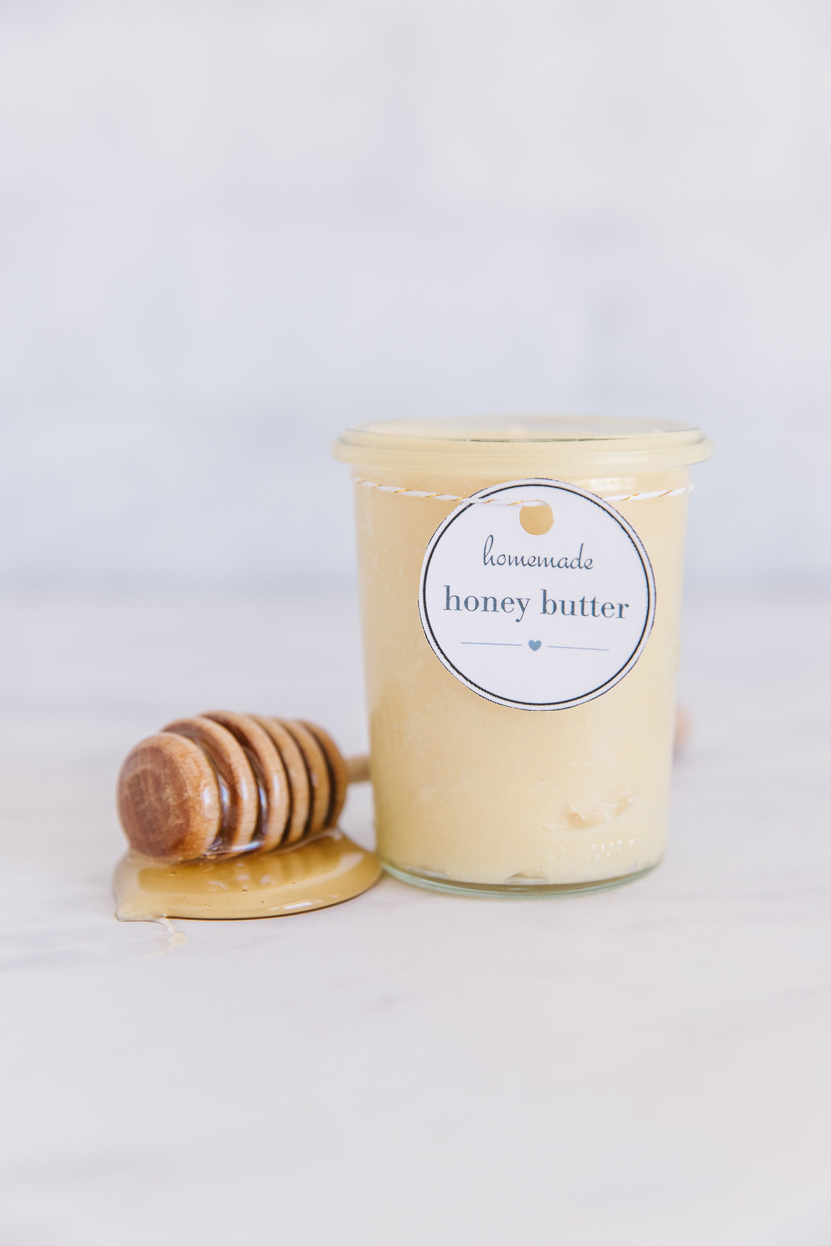 One container of homemade honey butter with label and a dollop of honey with a honey wand on the side.