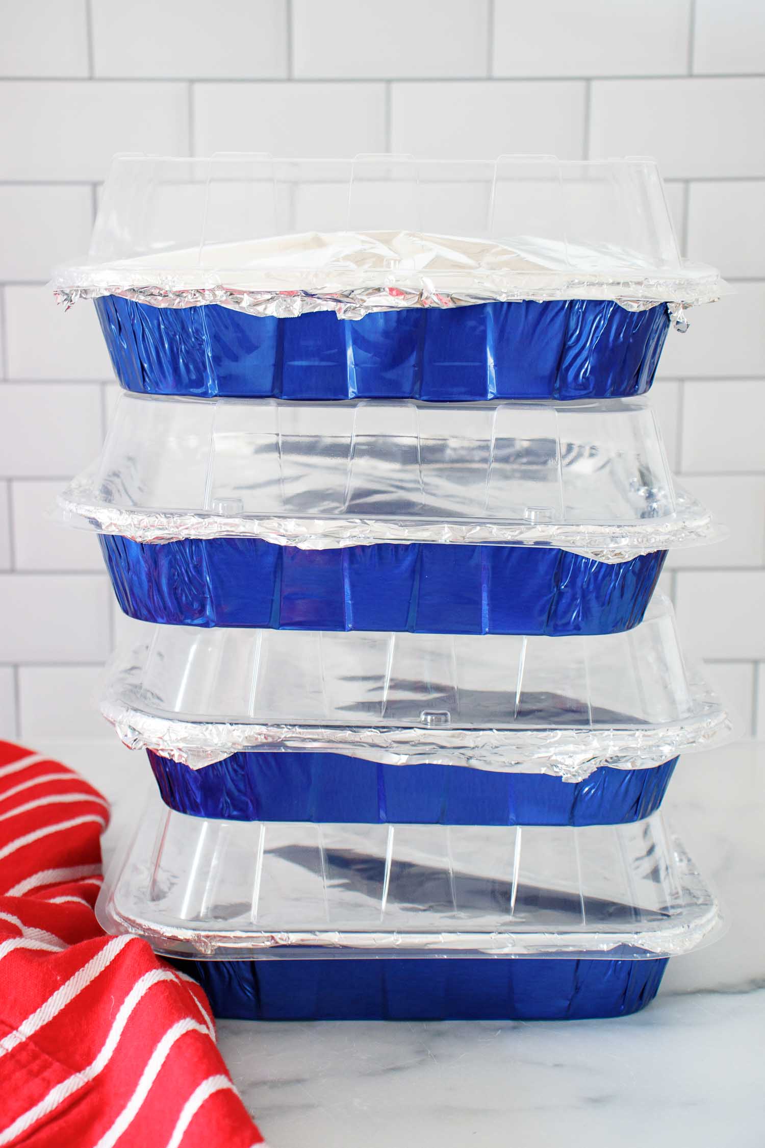 4 stacked blue aluminum foil baking pans filled with freezable apple crisp.