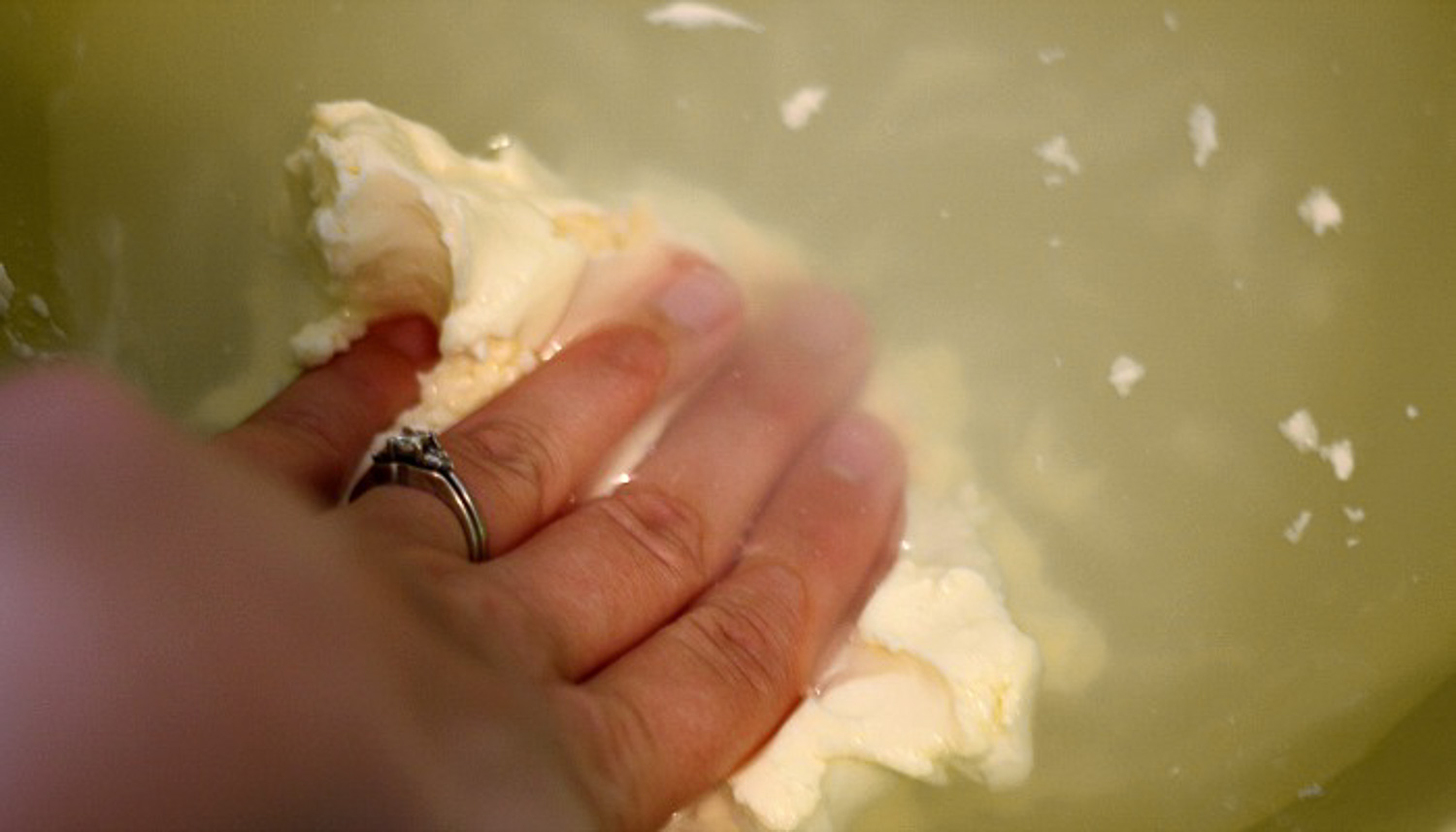 A hand with a ring pushing and washing the butter in water.