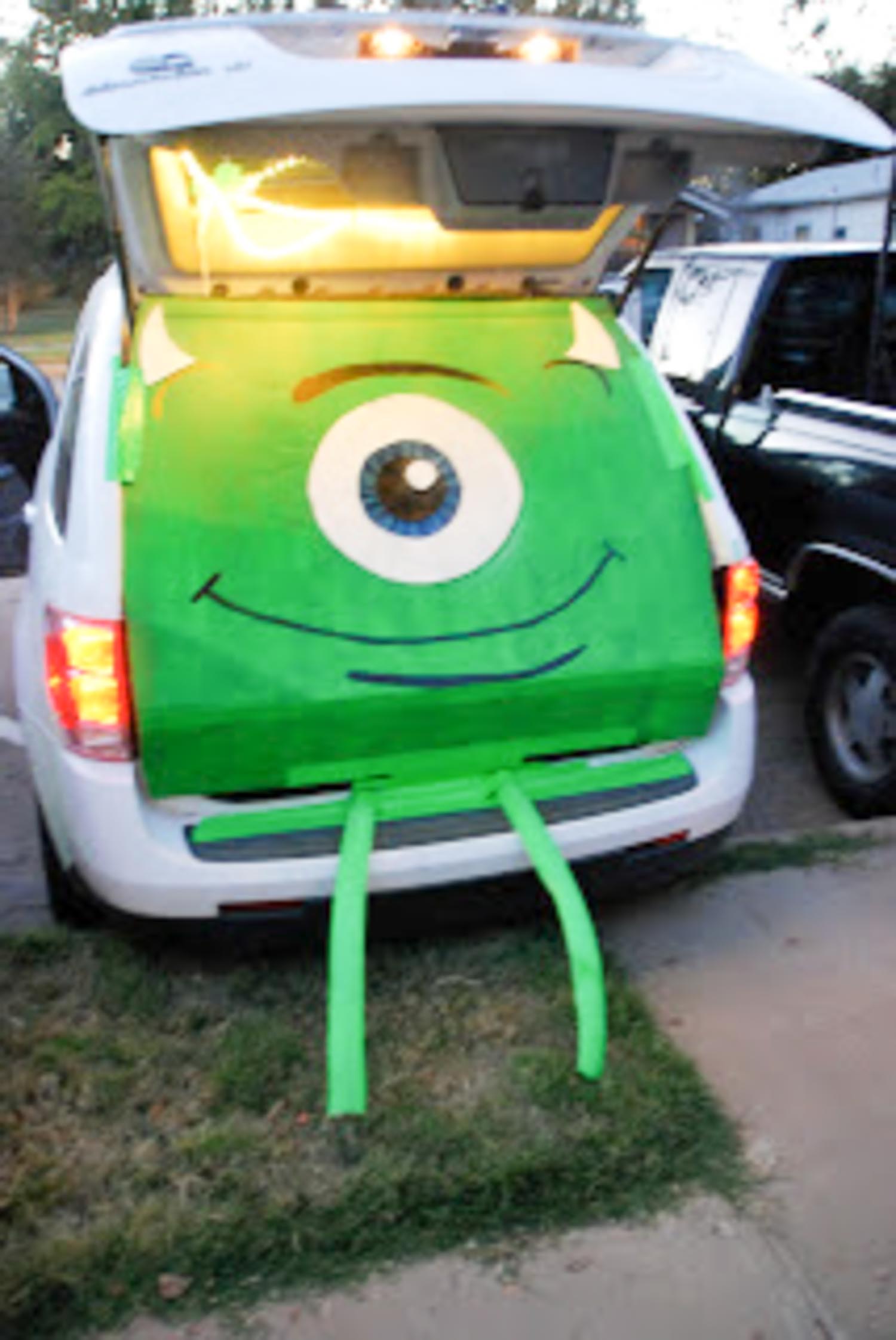 An open trunk with a green paper with a big eye and a big smile on it with legs hanging out of it.
