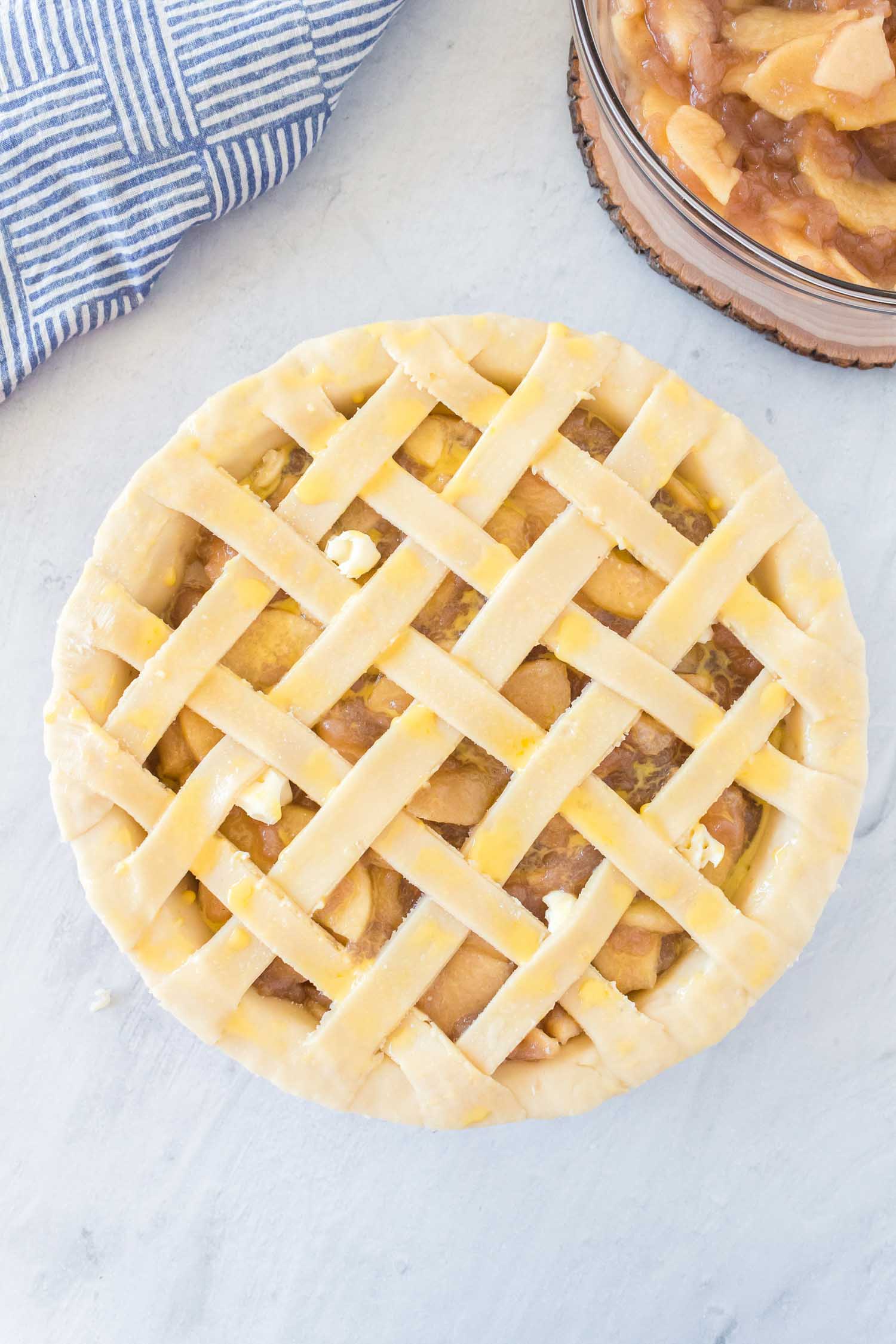 An unbaked apple pie with egg wash on it with apple pie filling on the side.