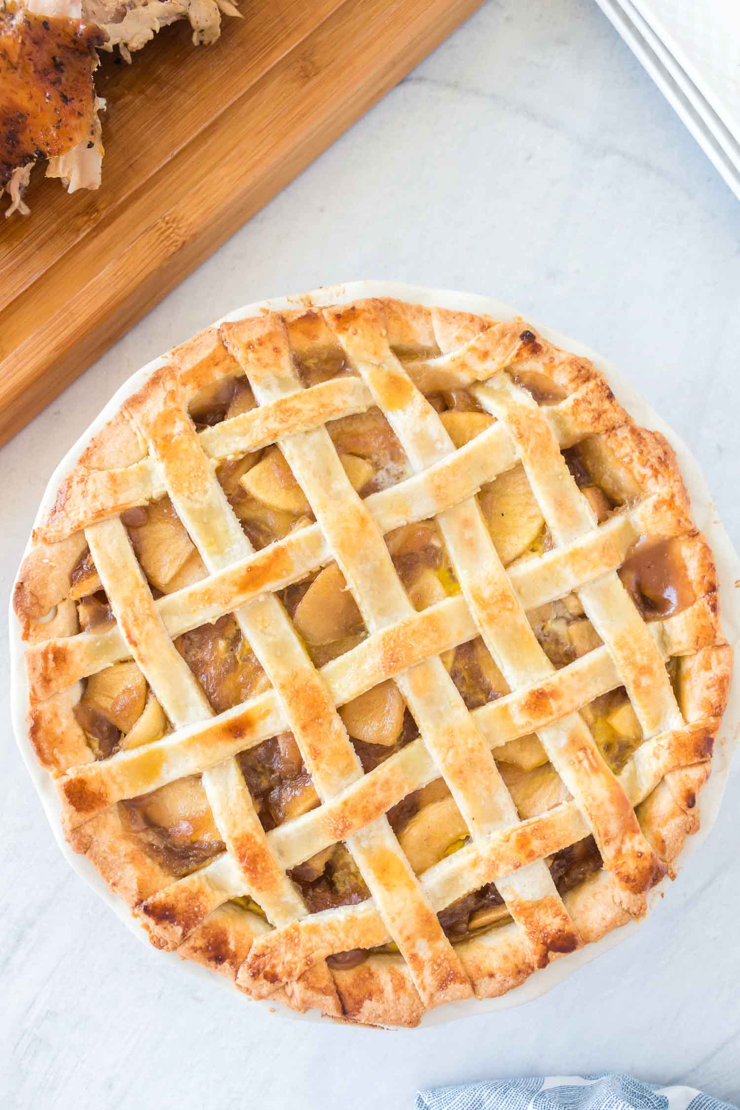 A baked apple pie with a wooden cutting board with turkey on it.