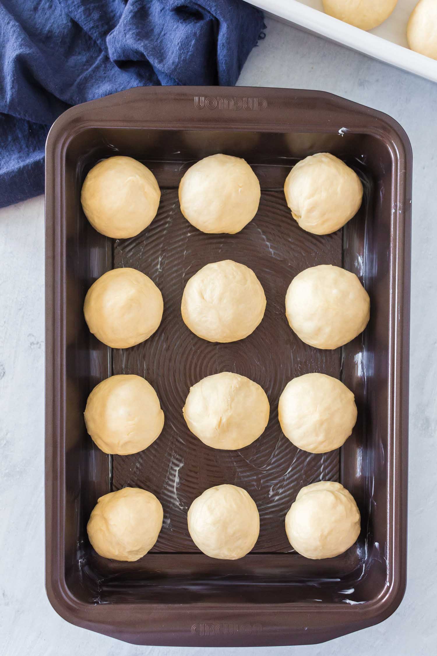 A dark nonstick buttered pan with 12 balls of uncooked dough.