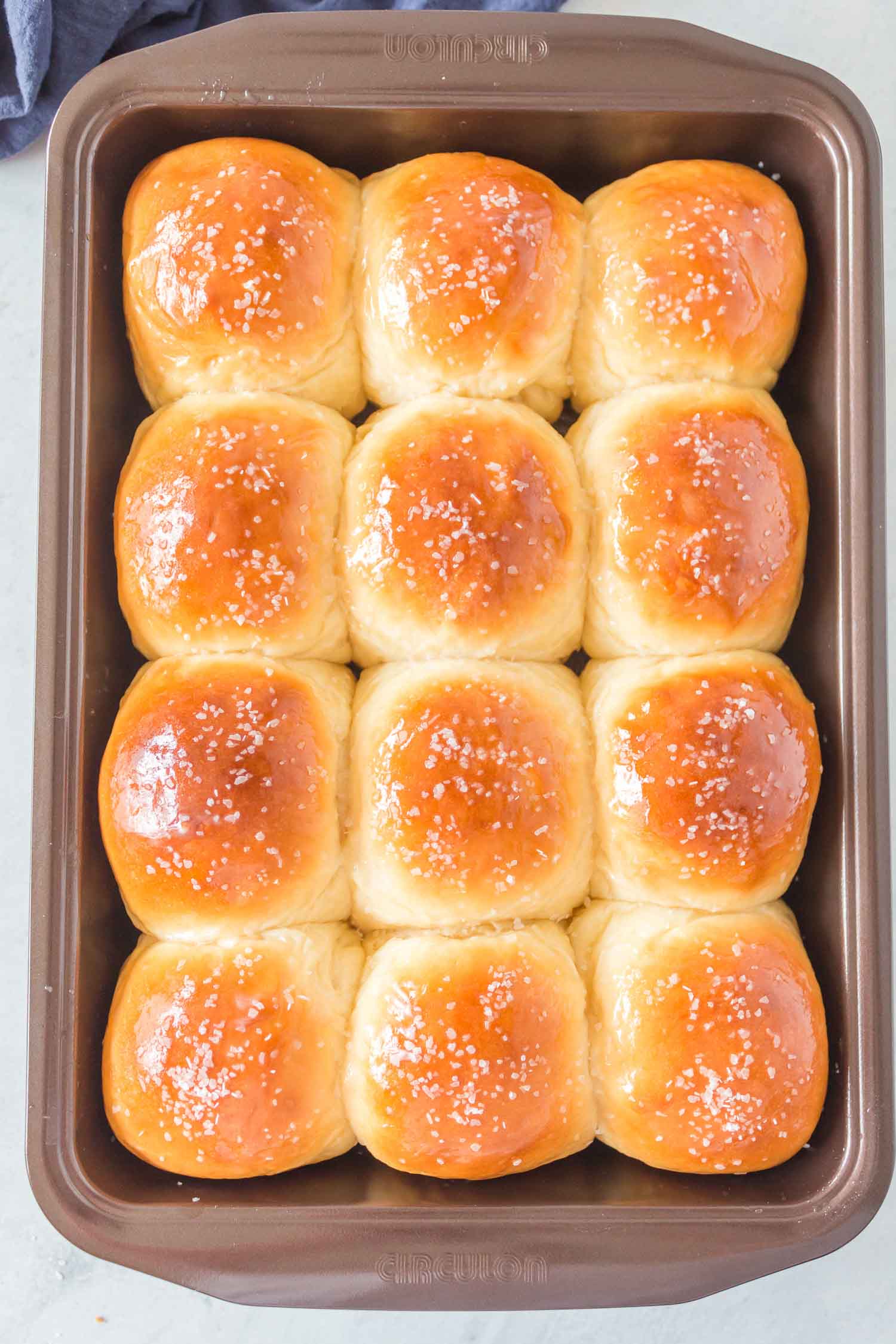 A dark nonstick pan with 12 cooked rolls that have been buttered and salted.