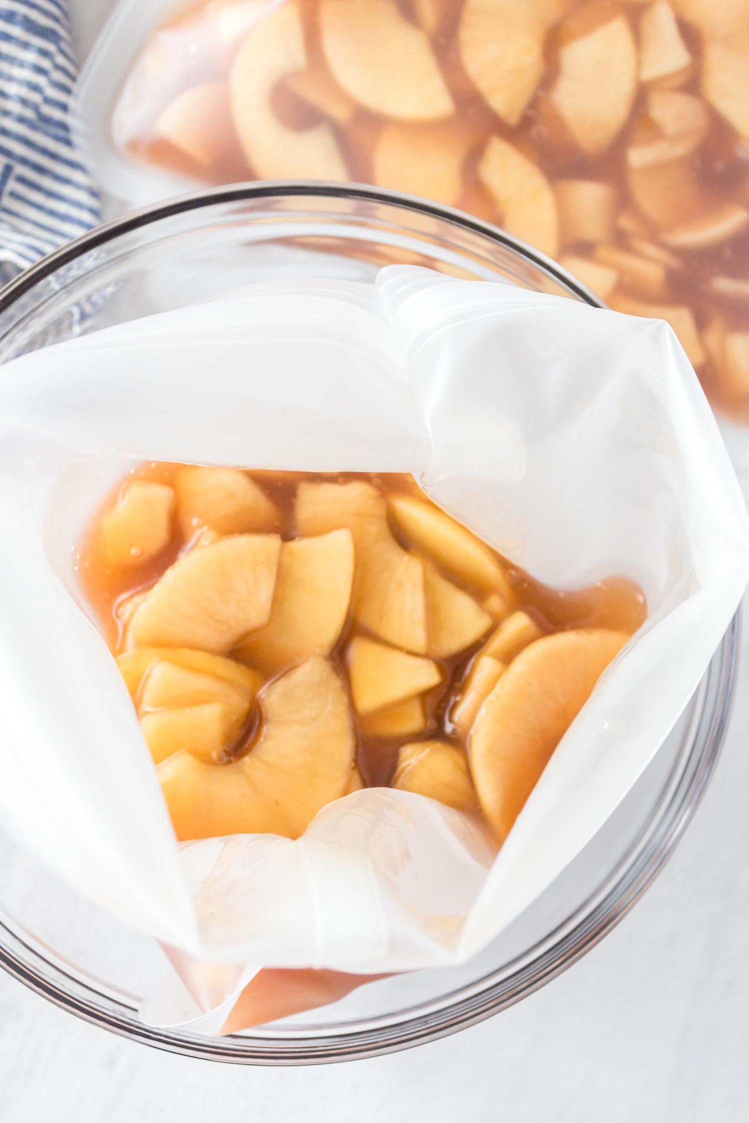 A resealable freezer bag with make ahead apple pie filling in a glass bowl with other filled bags on the side.
