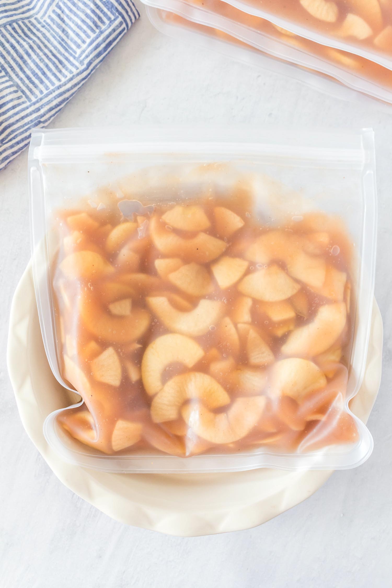 A resealable freezer bag full of apple pie filling in a white pie pan.
