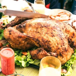 Knife cutting a savory roasted turkey set on a platter with greens.