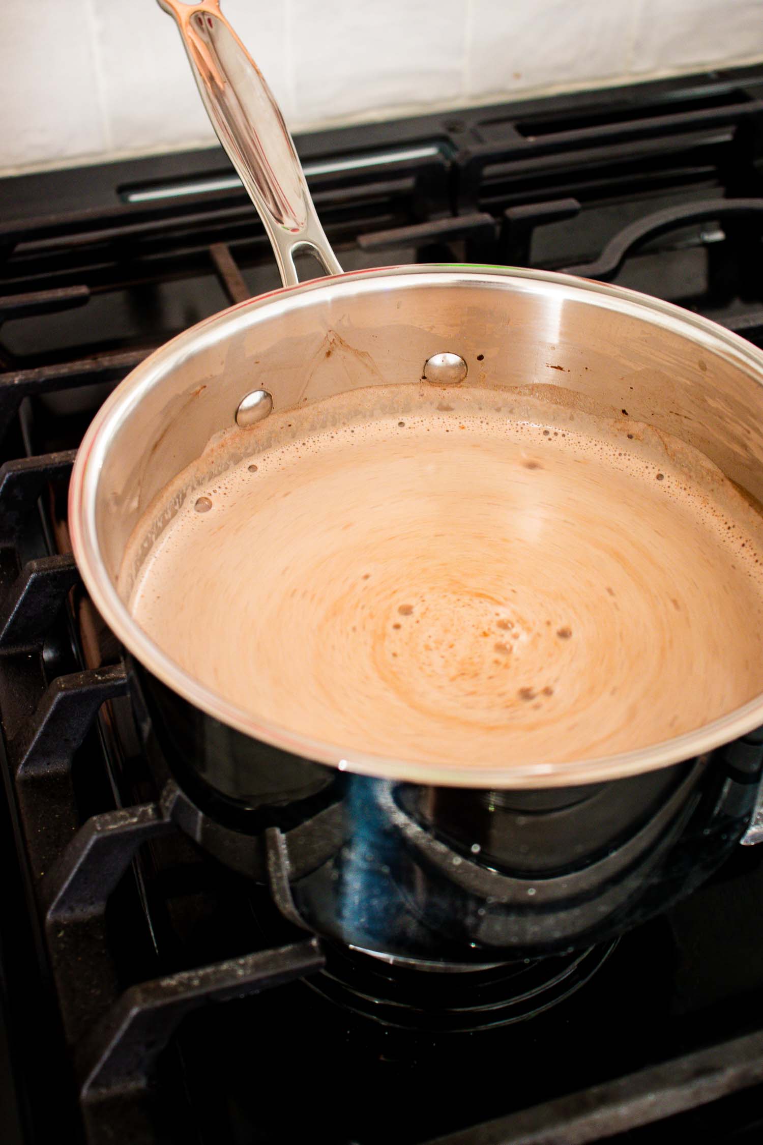 A metal pan on a stove with hot chocolate in it.