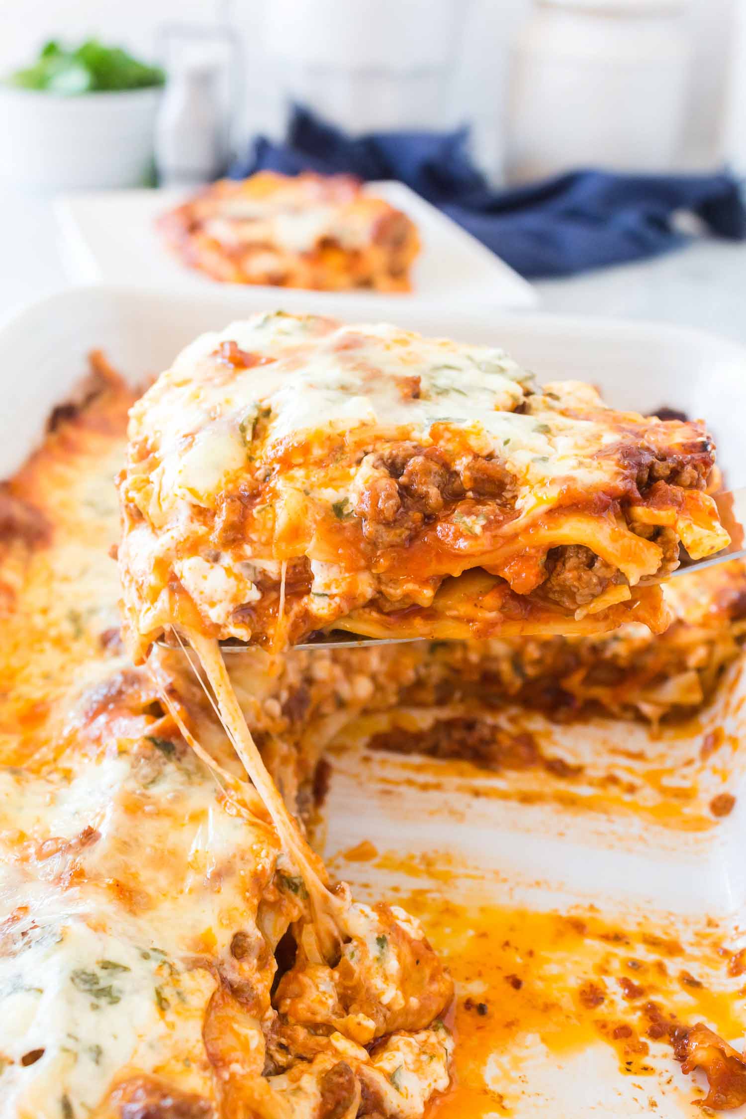 A white dish of lasagna with a serving taken out with a metal spatula.