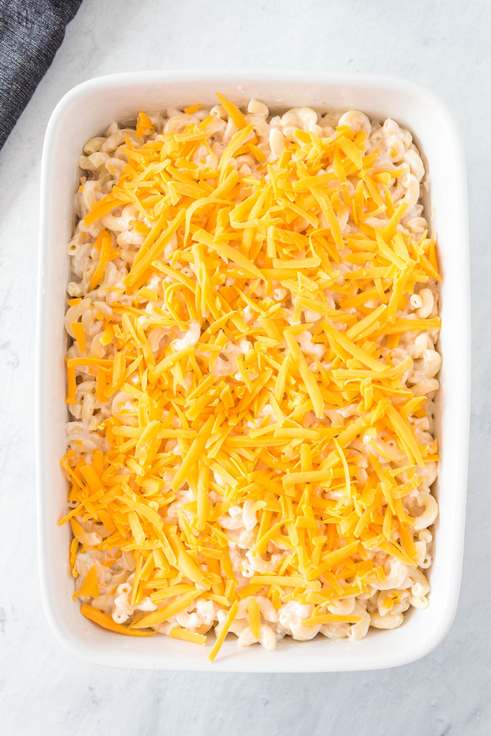 A white dish of unbaked casserole with shredded cheese on top.