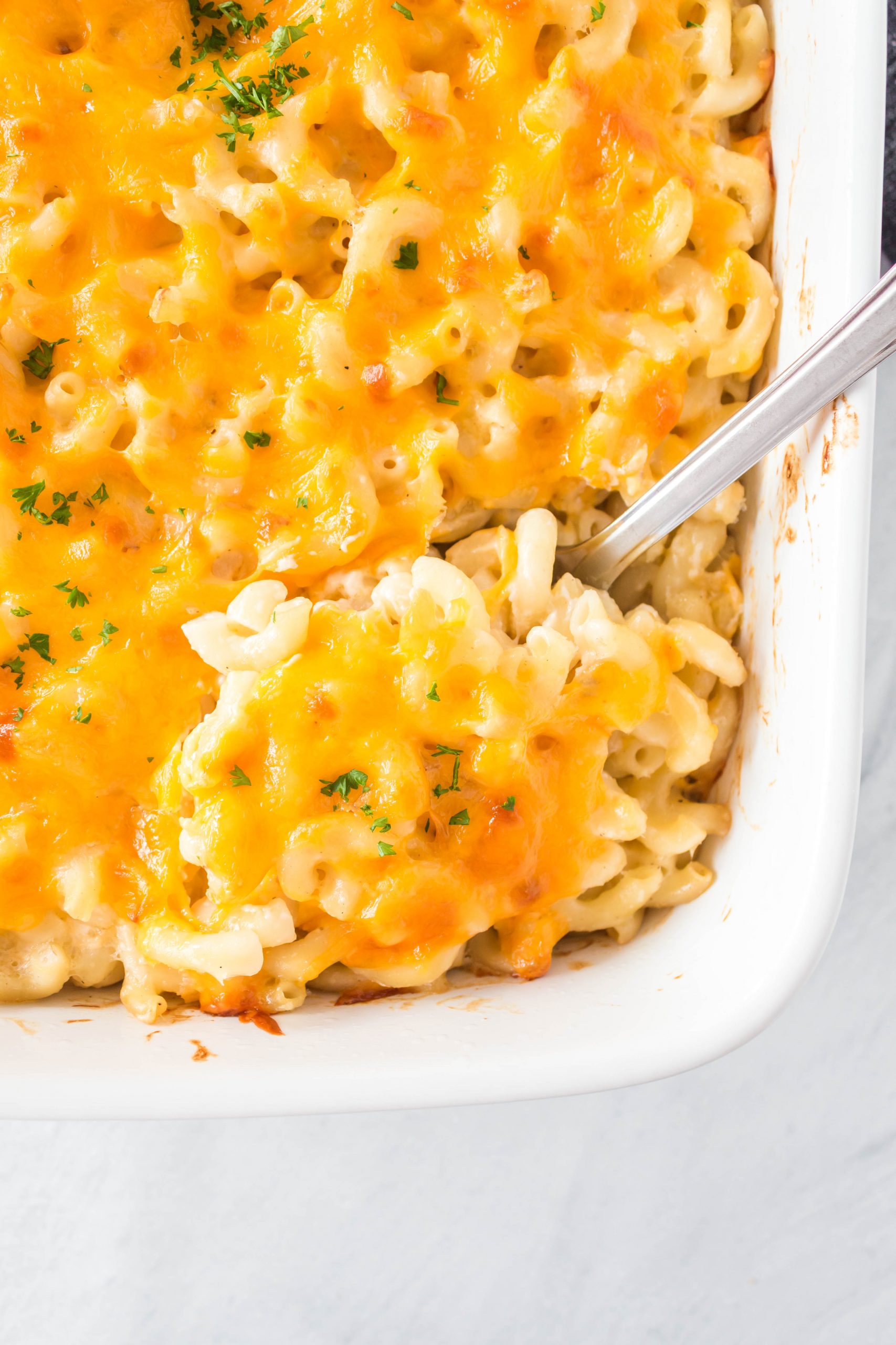 A white casserole dish with a metal spoon spooning out tuna macaroni casserole.