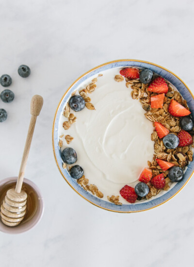 Bowl of Greek yogurt topped with granola and fruit next to a jar of honey.