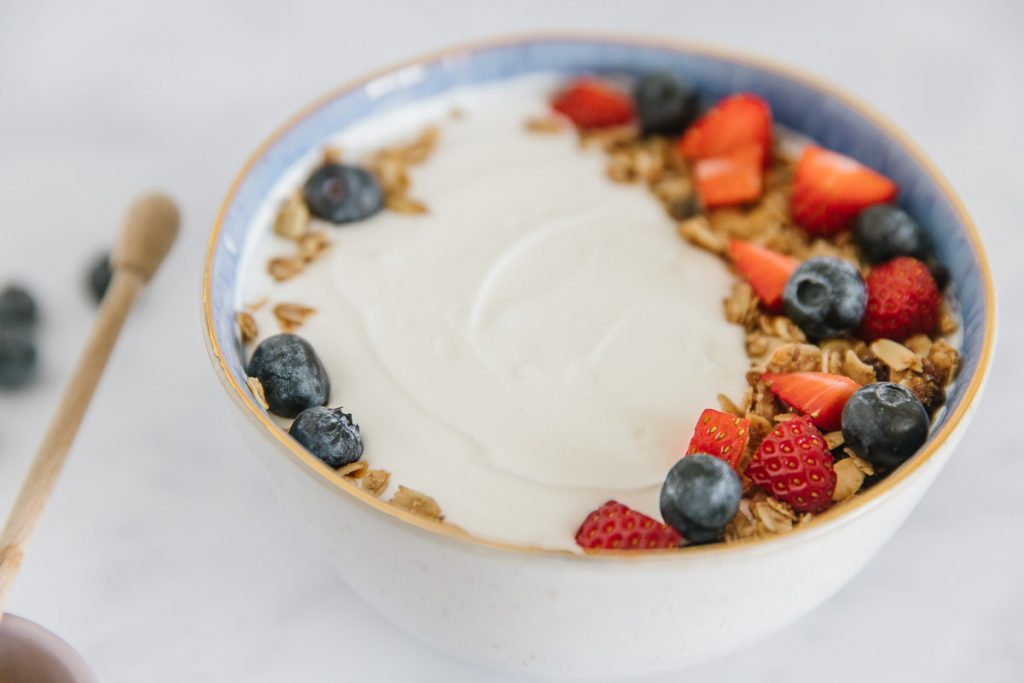 Bowl of Greek yogurt topped with granola and fruit.