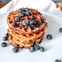 Stack of blueberry chaffles on a white plate with blueberries.
