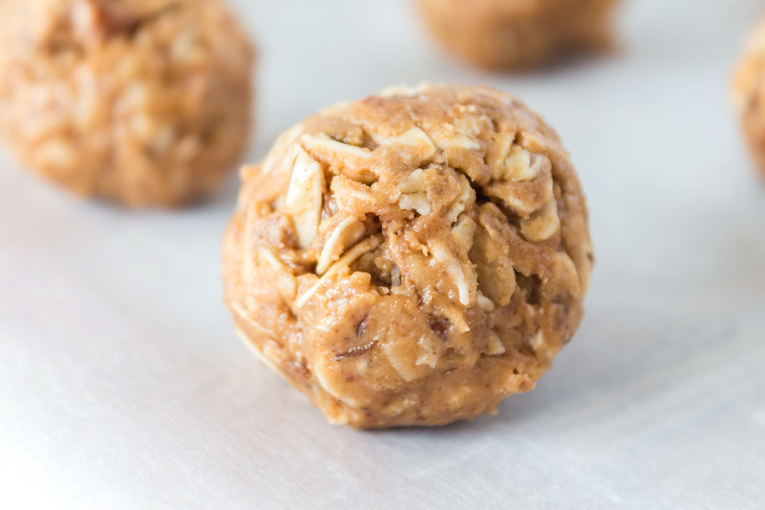 A peanut butter protein ball on parchment paper with other ones lined behind it.
