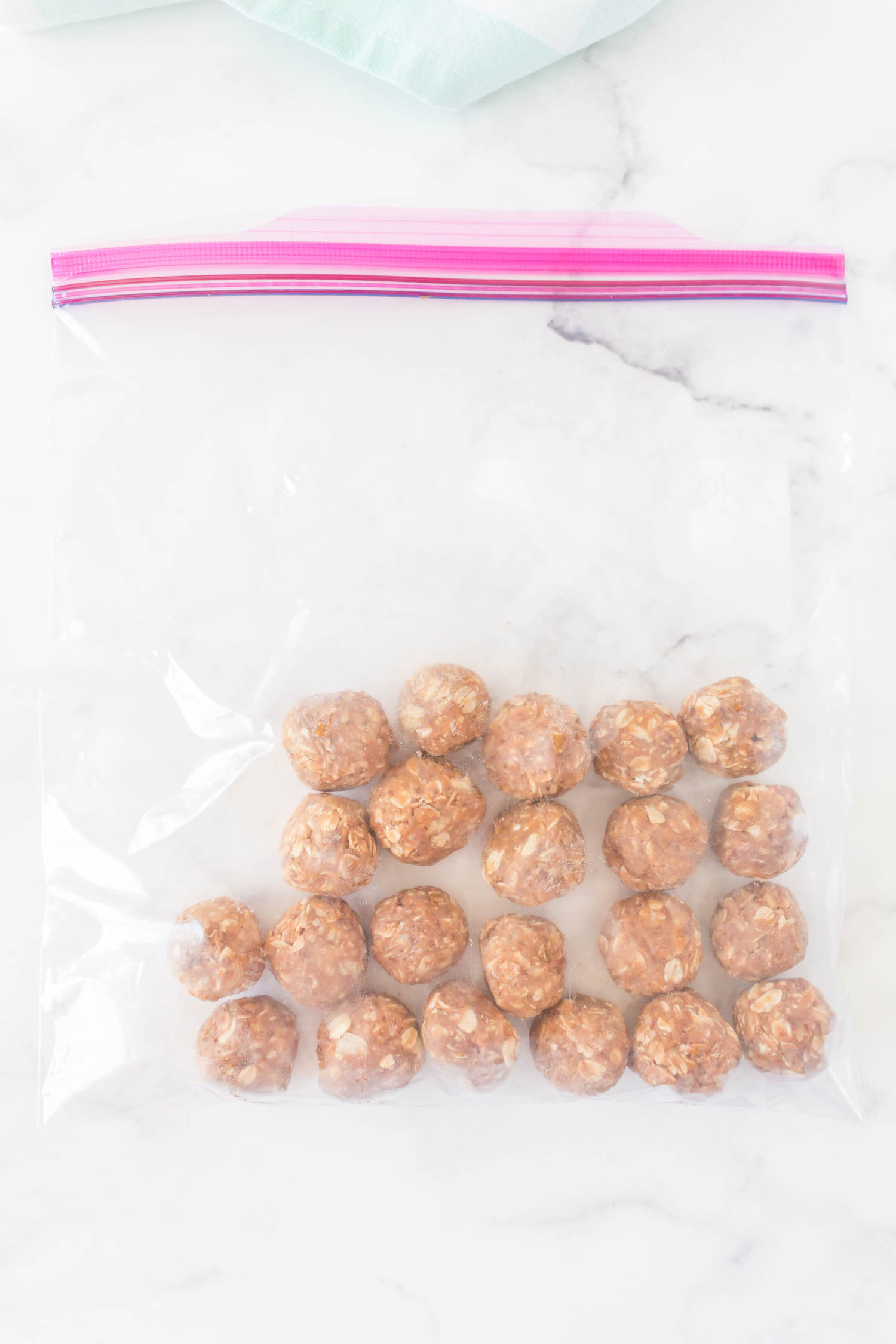 A large resealable bag with energy balls in it on a white counter.