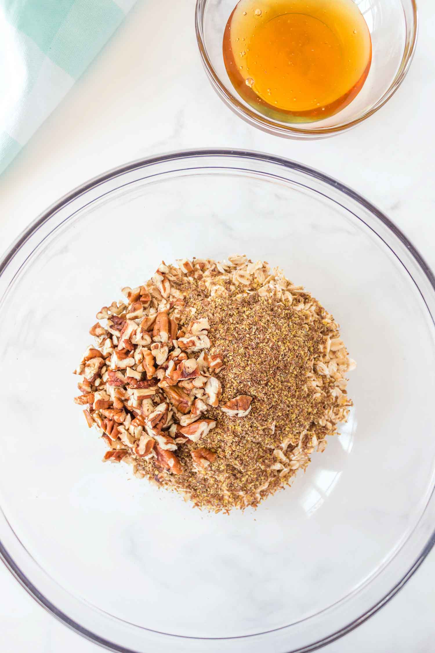 A large glass bowl of oatmeal with spices and pecans in it with a small glass bowl of honey behind it.