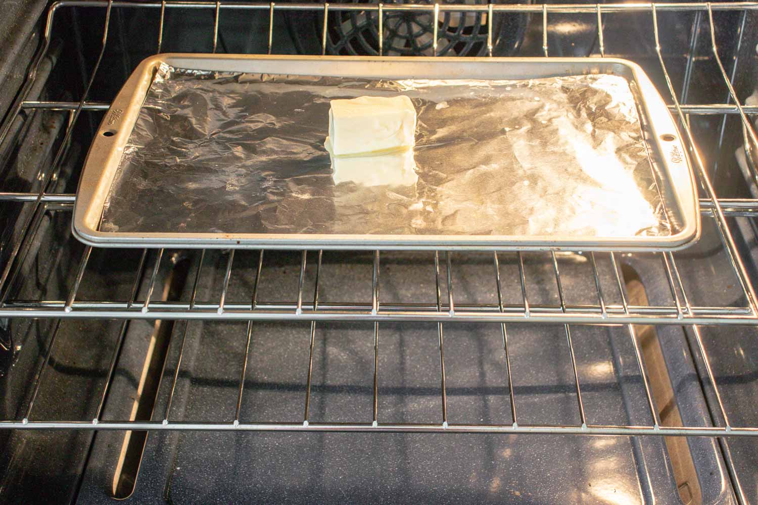 A metal pan with foil with a stick of butter on it in an oven.
