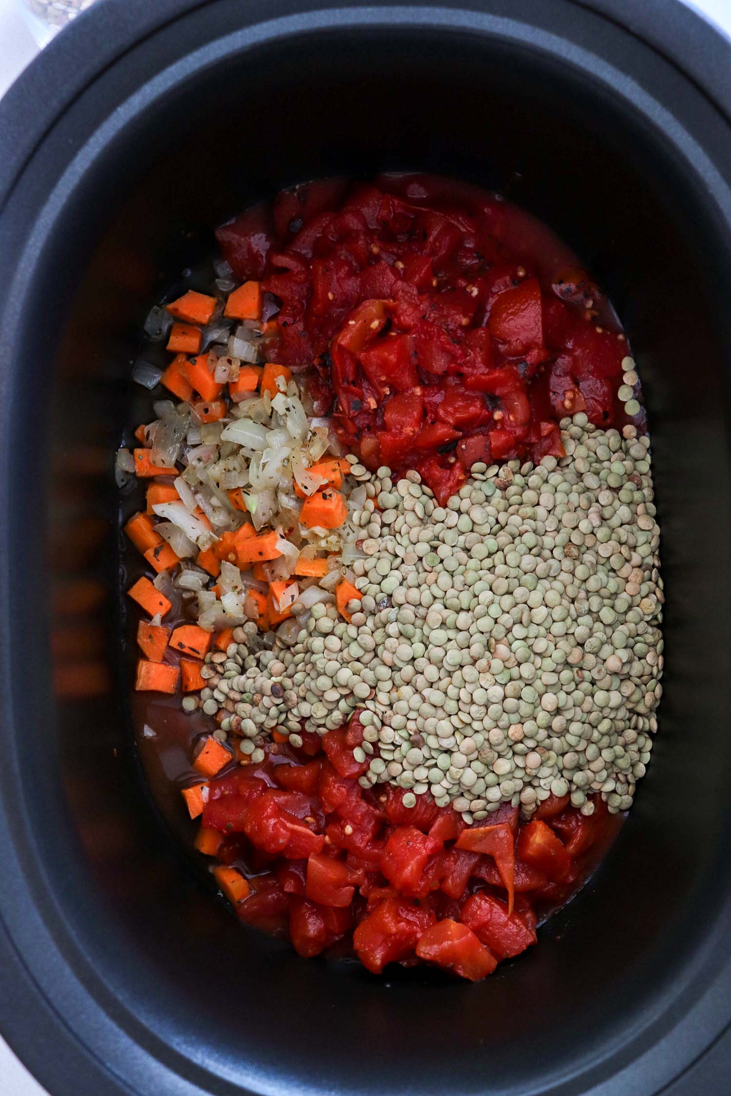 A black slow cooker with ingredients in it to make Bolognese sauce.