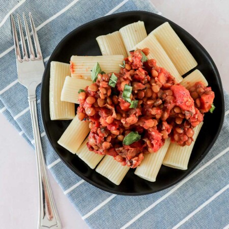 Lentil Bolognese over large noodles on a black plate.