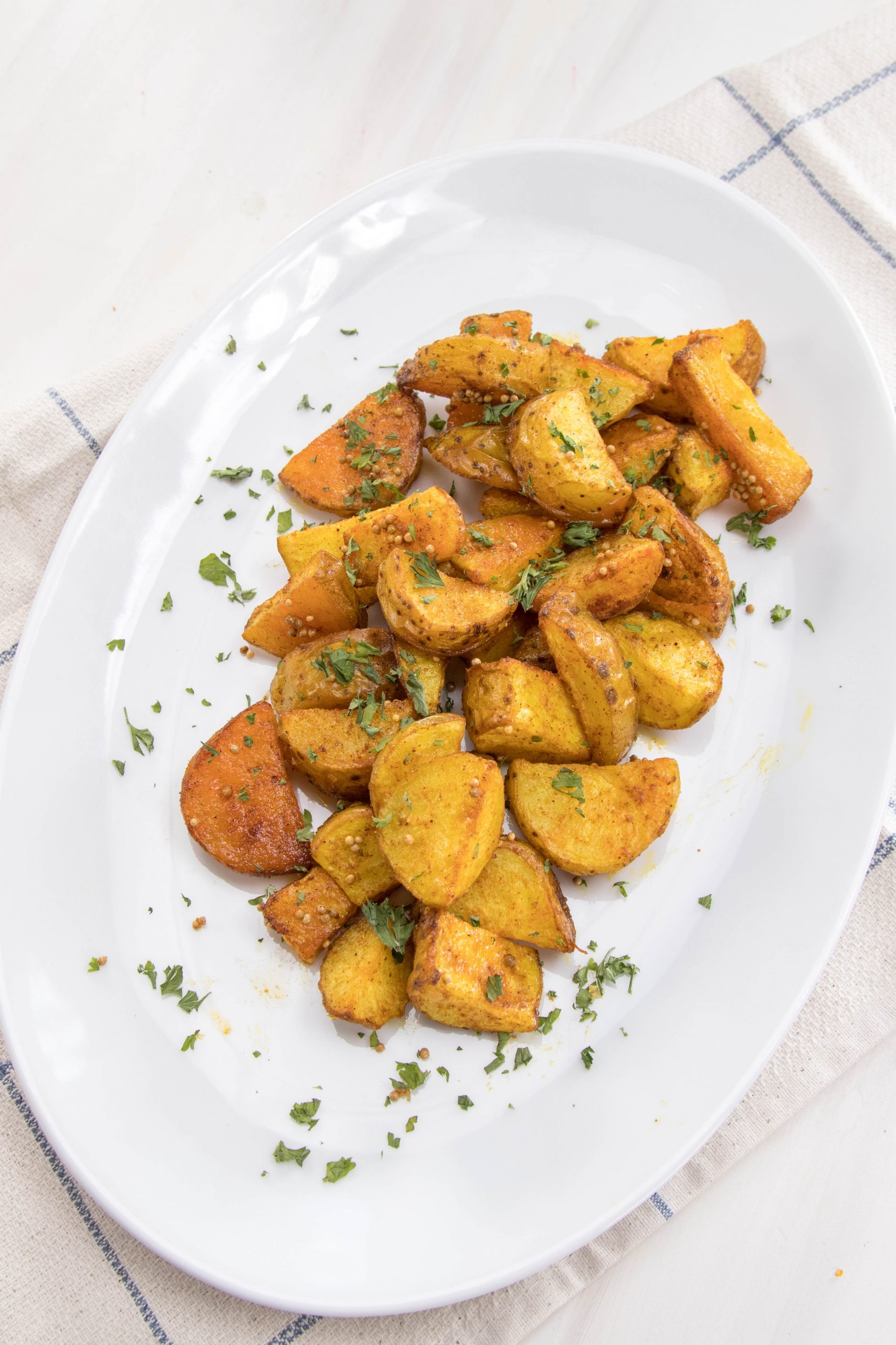 An oval white plate with roasted potatoes and herbs.