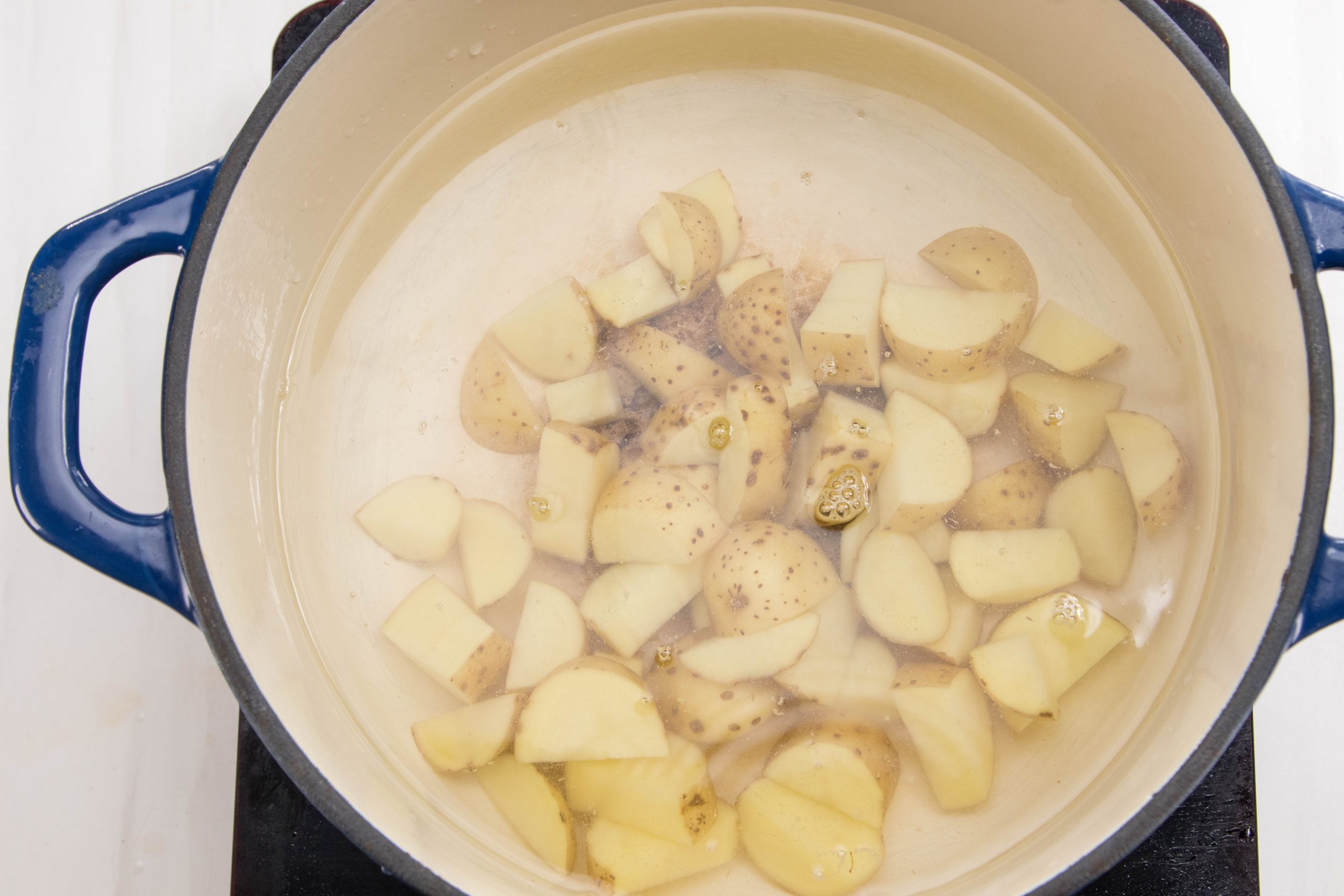 A blue Dutch oven pot filled with water and cut potatoes.