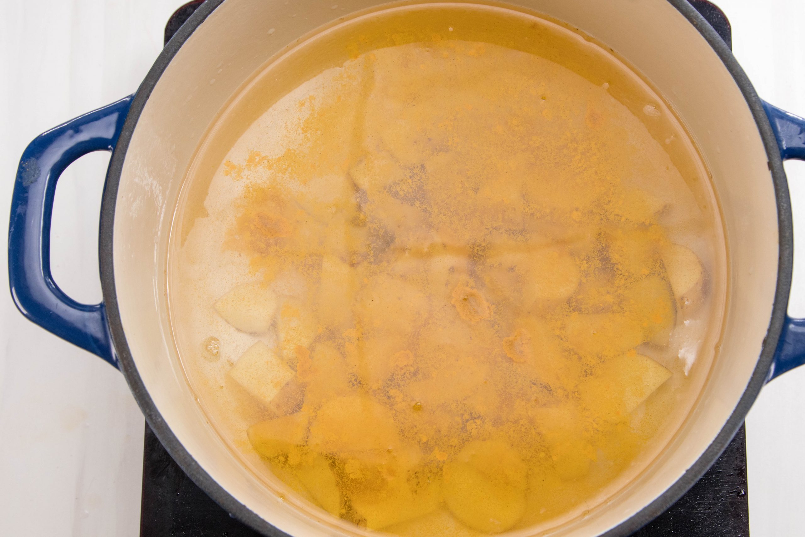 A blue Dutch oven pot filled with water, seasonings and cut potatoes.