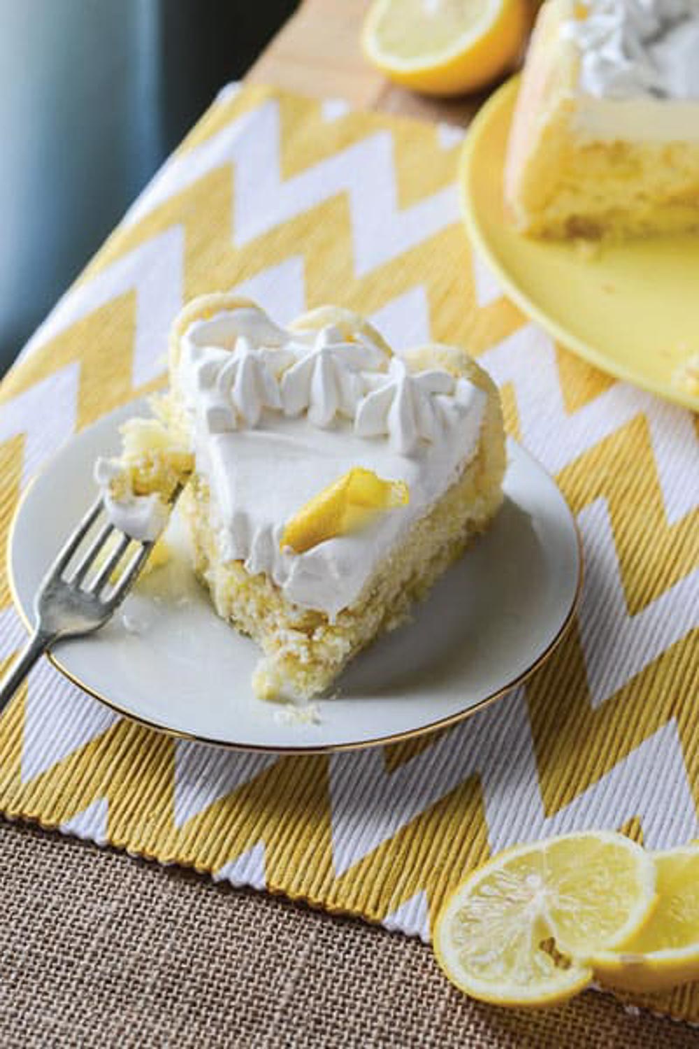 A cake on a yellow plate with a slice cut out of it and one slice on a white plate with a metal fork in it with a bite on it.