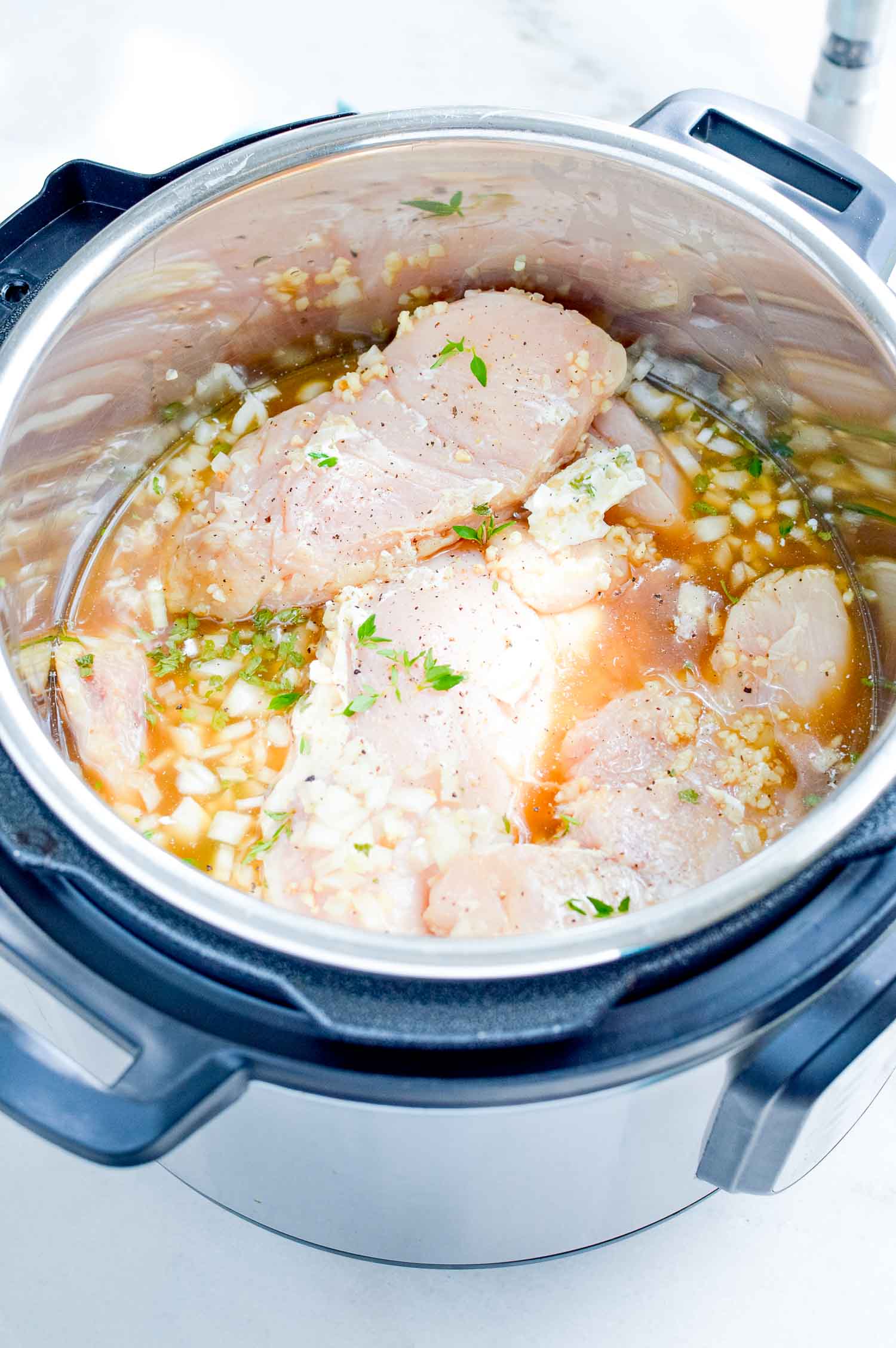 An instant pot with ingredients with chicken, veggies and herbs with stock filling the pot.