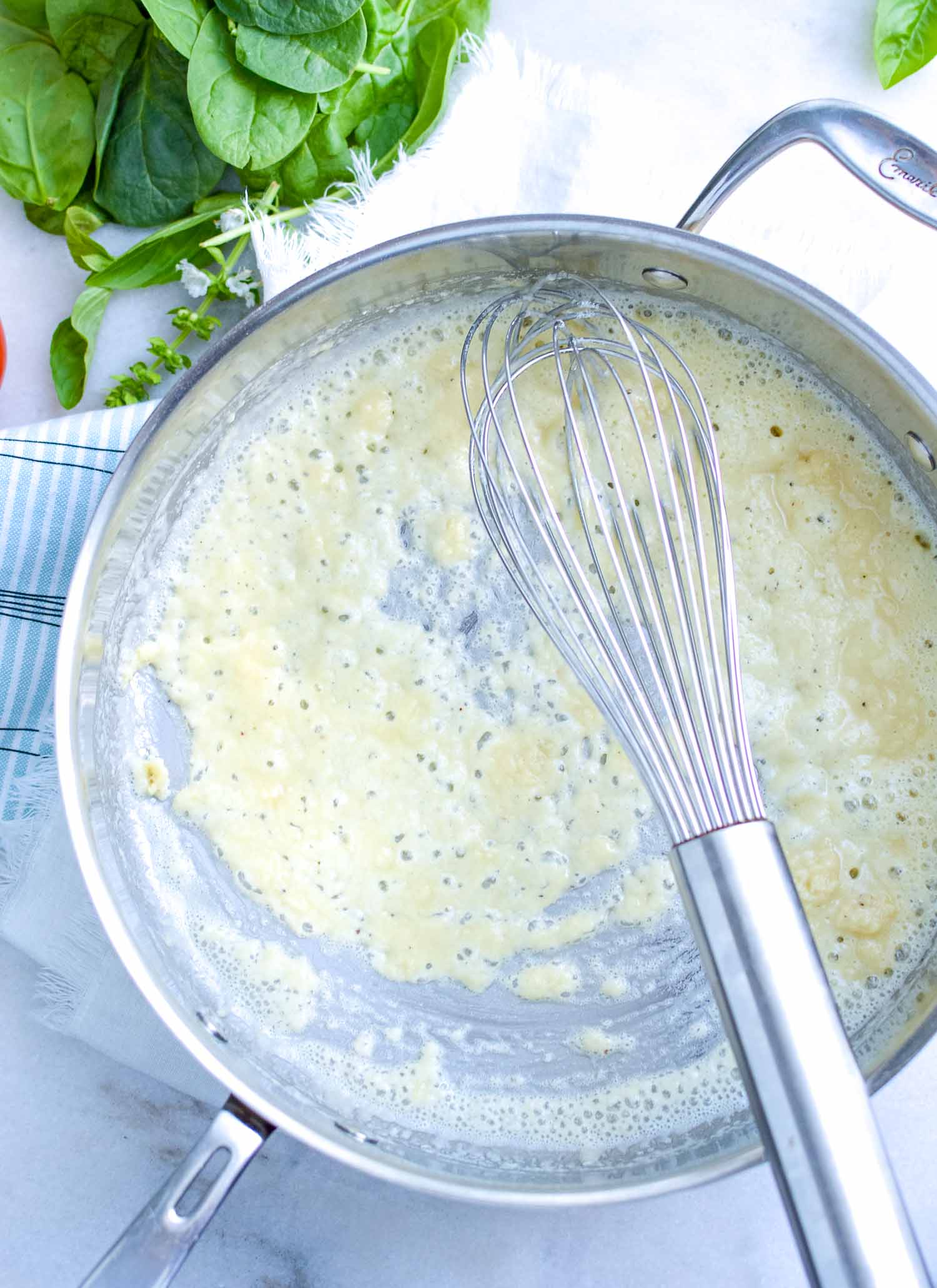 A silver pan with white sauce in it with a silver whisk in it.