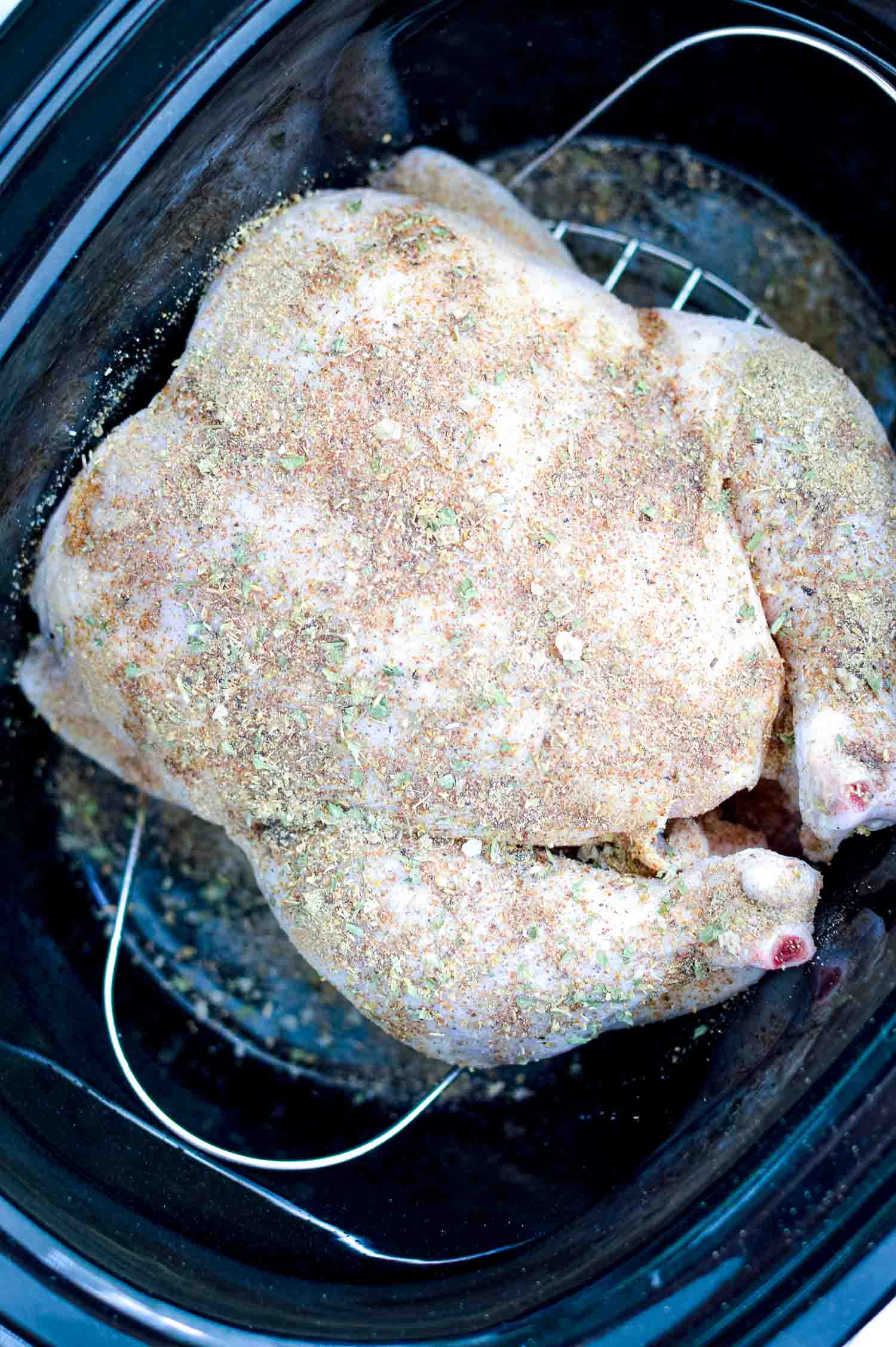 A slow cooker with a raw whole chicken rubbed with spices on it.