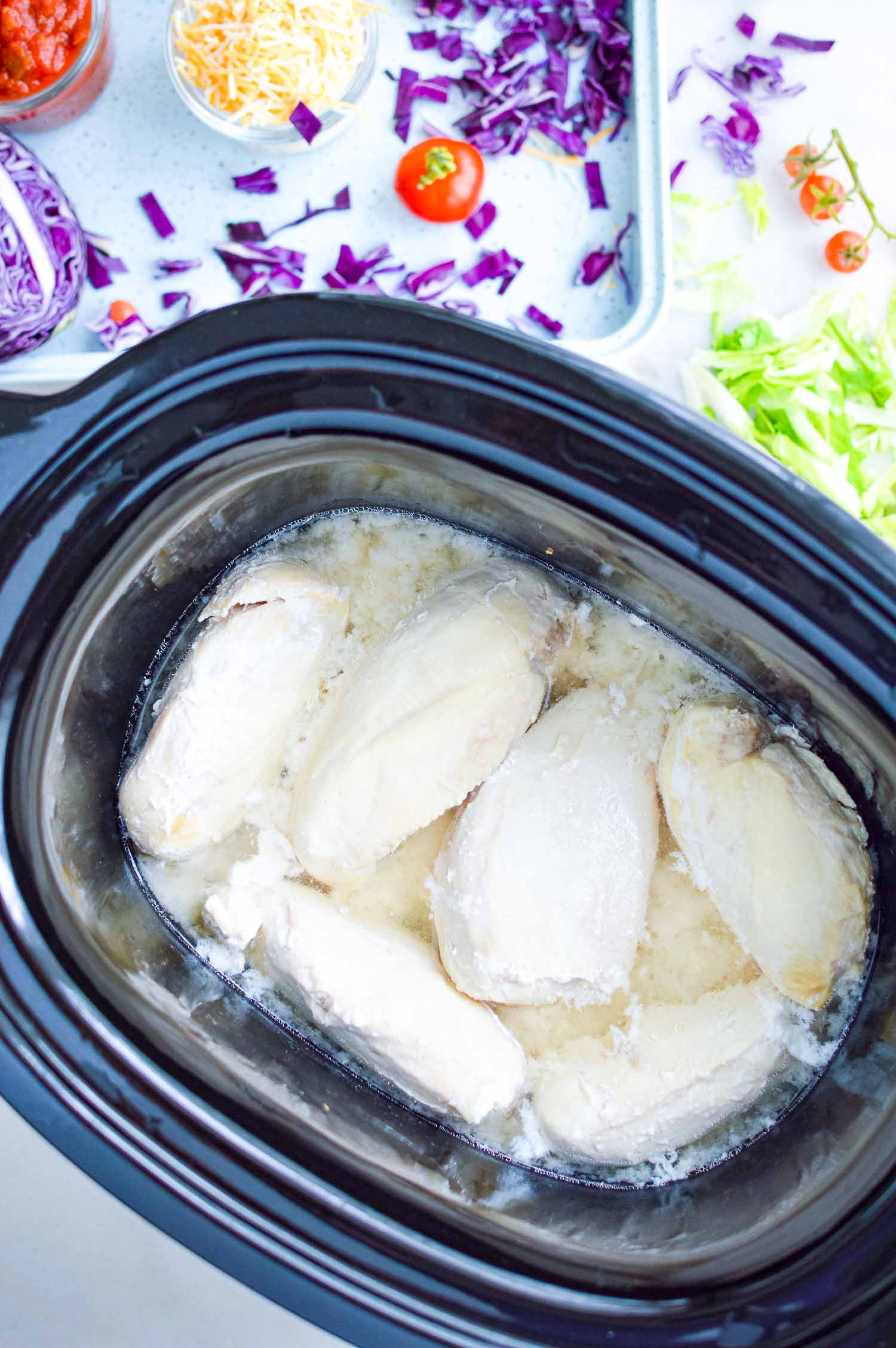 A black crockpot with cooked whole chicken breasts in it.