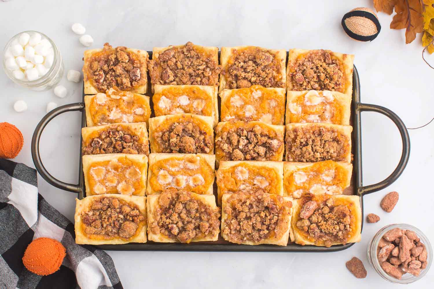 A pan filled with dessert pastries laid together with glass cups of marshmallows and pecans and leaves around it.