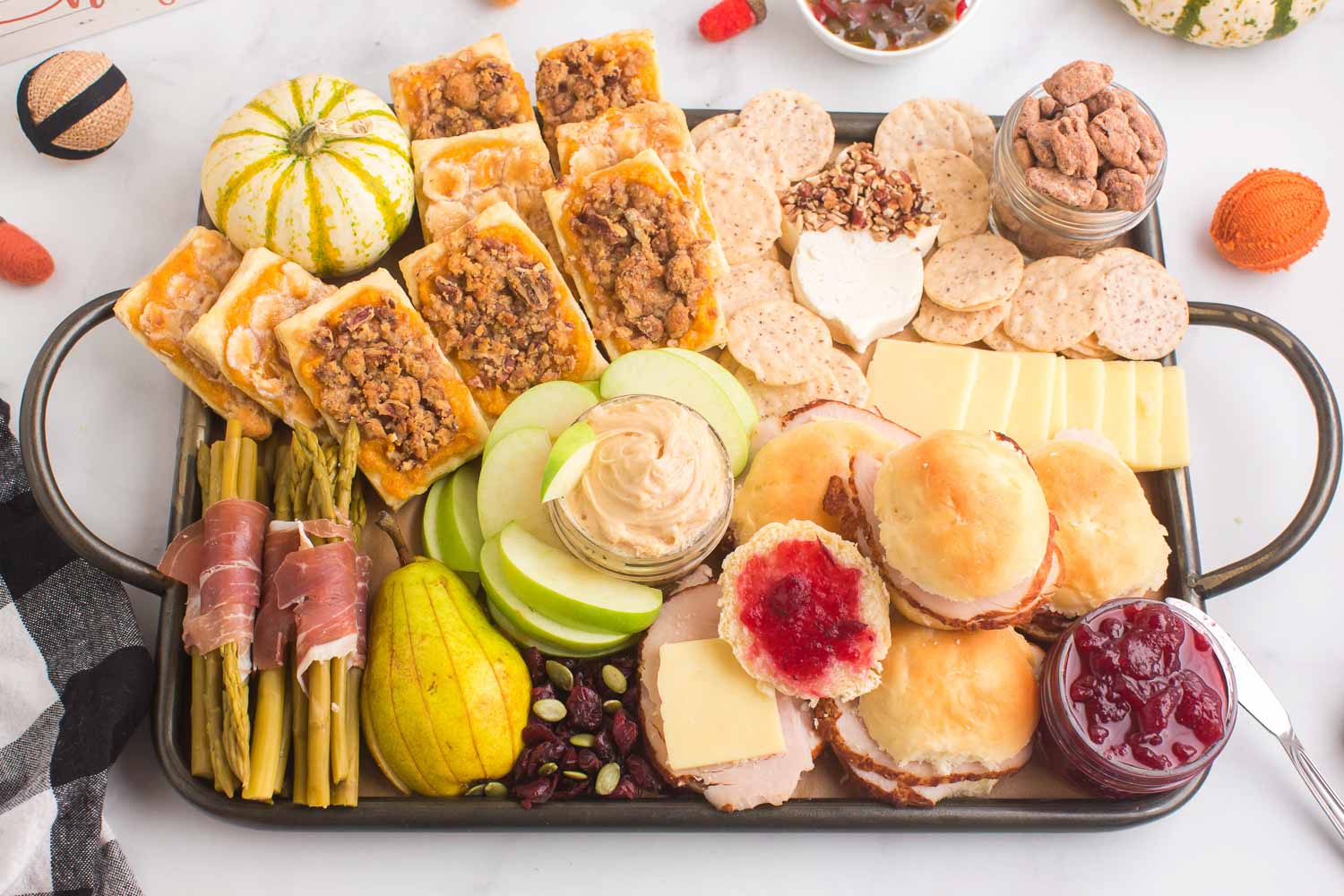 A Thanksgiving charcuterie board with pastries, fruit, dips, rolls, meat, asparagus, and nuts on it.