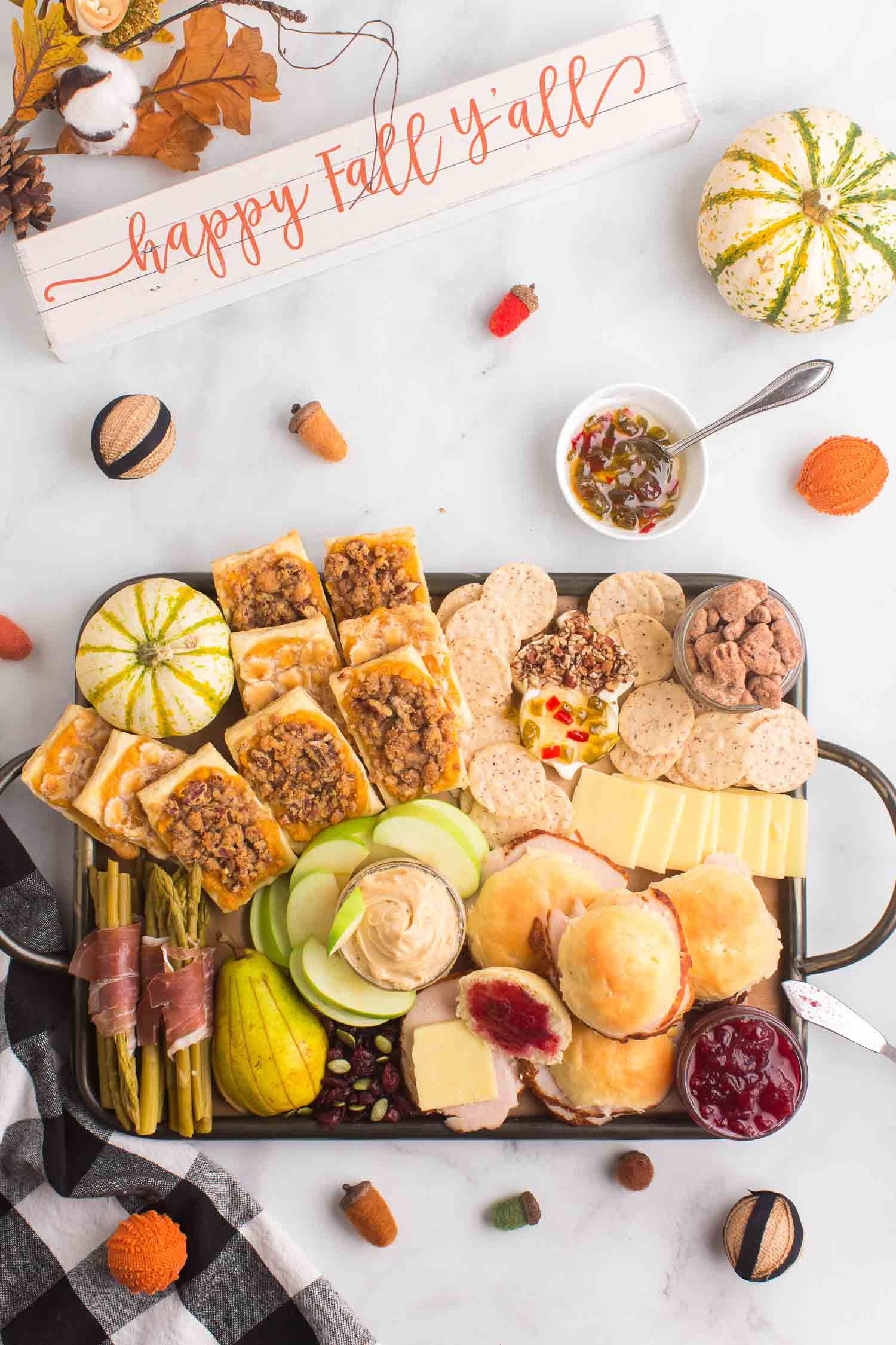 A full Thanksgiving charcuterie board with décor around the board and a bowl of pepper jelly with a silver spoon in it.