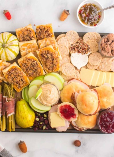 Charcuterie board stuffed with crackers, fruits, spreads, gourds, and more.
