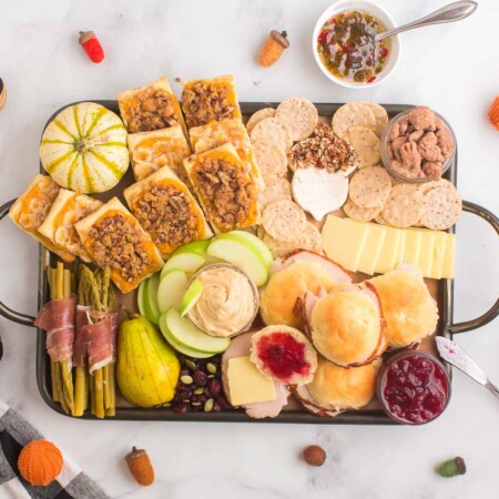 Charcuterie board stuffed with crackers, fruits, spreads, gourds, and more.