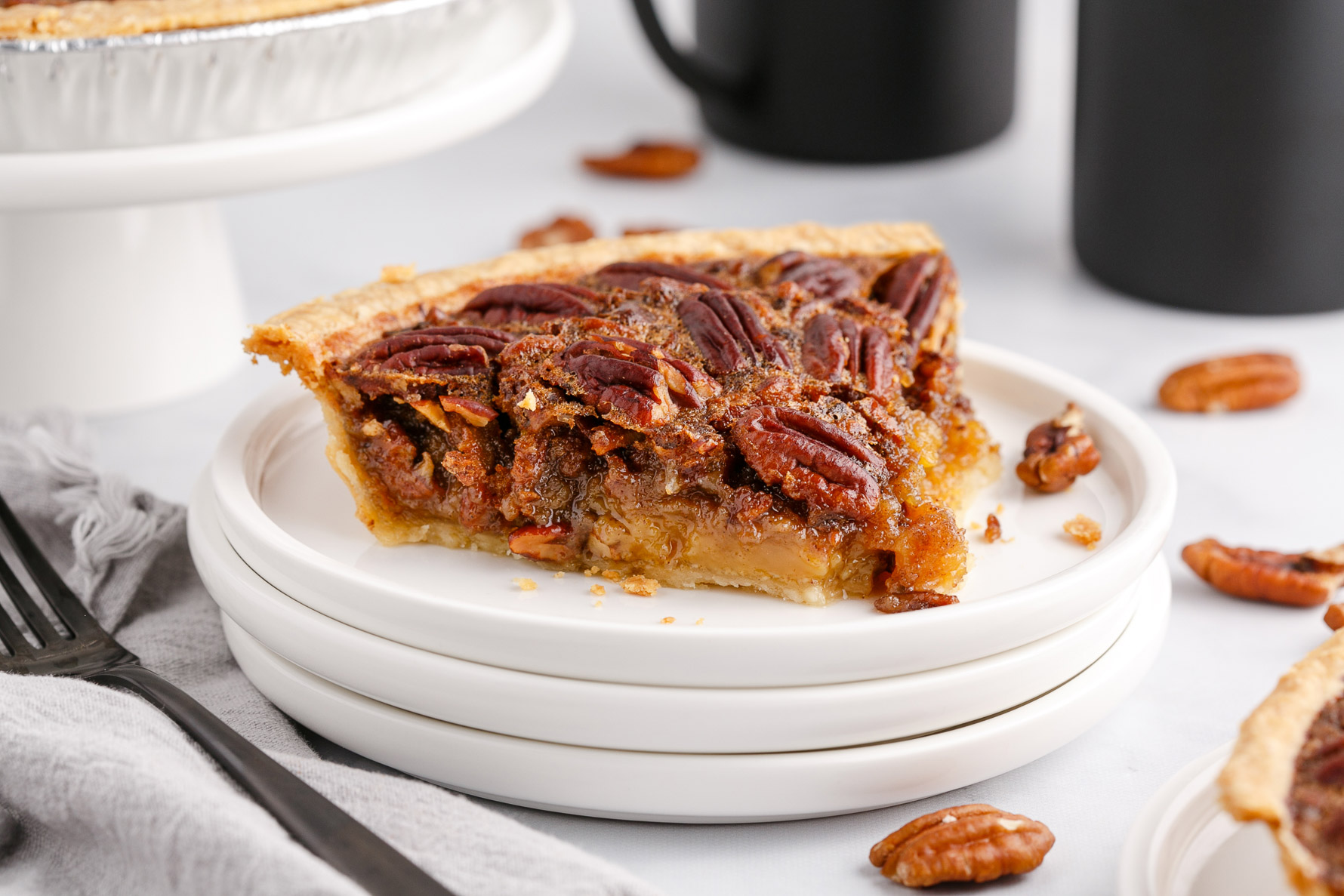 Three white plates with a slice of pie on it with a silver fork and pecans around it.