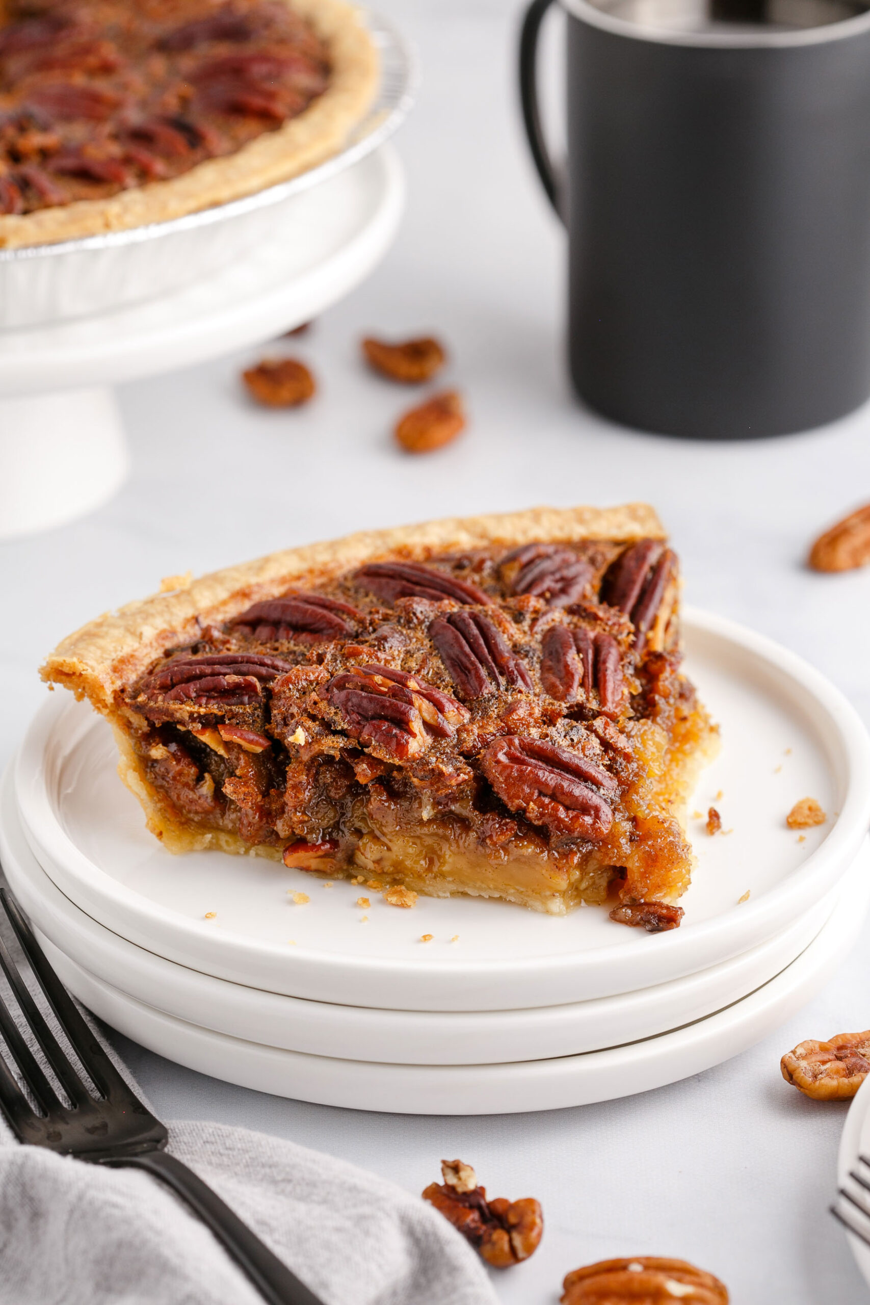 A slice of pie on top of three white plates with a fork on the side with pecans scattered around.