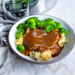 Cube steak with gravy in a bowl with broccoli and mashed potatoes.